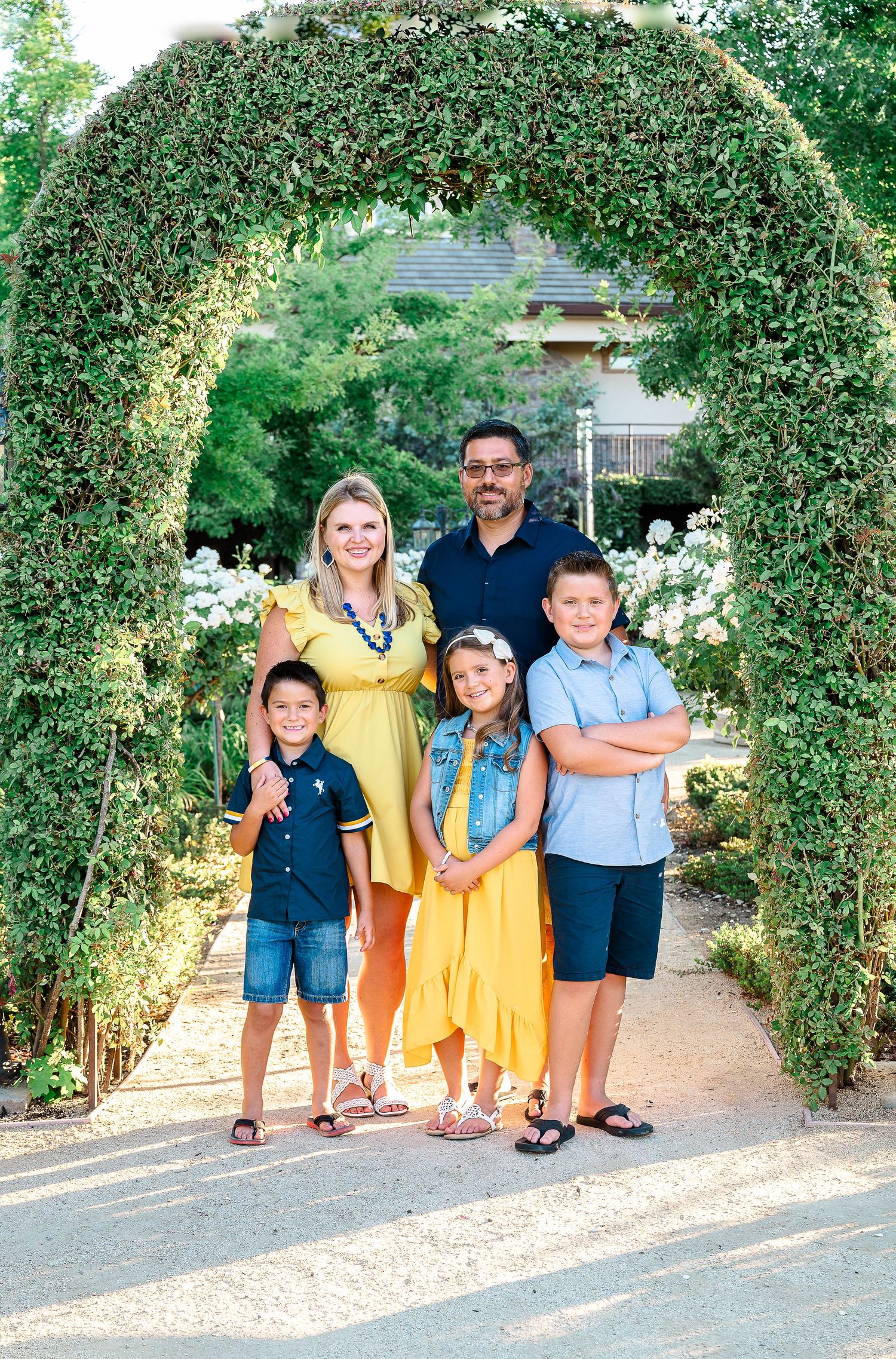 Family of 5 dressed in blues and yellows posed under a green arch