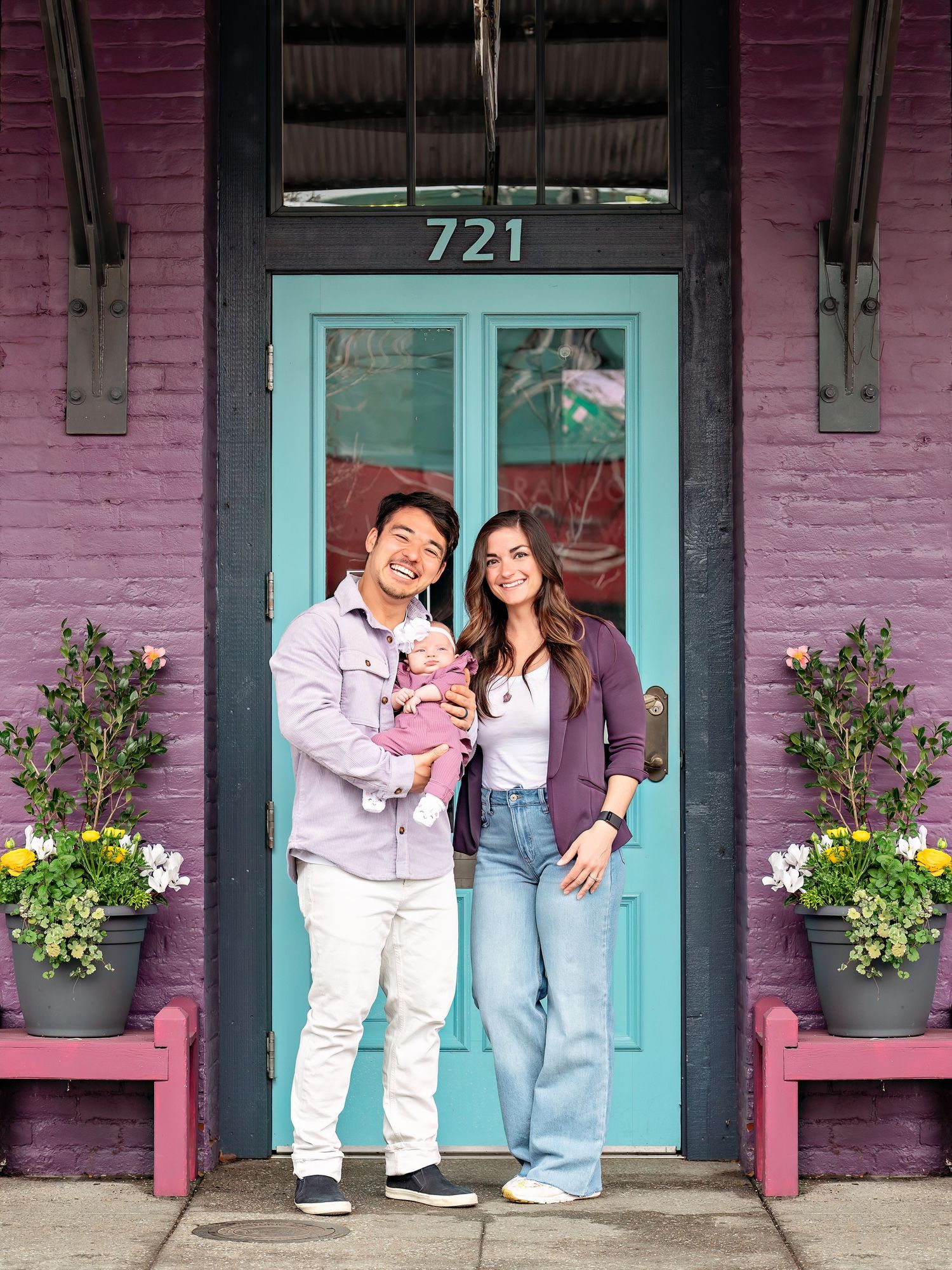 Young couple with a baby in front of a teal door on a purple building.  Taken in downtown Folsom, California.