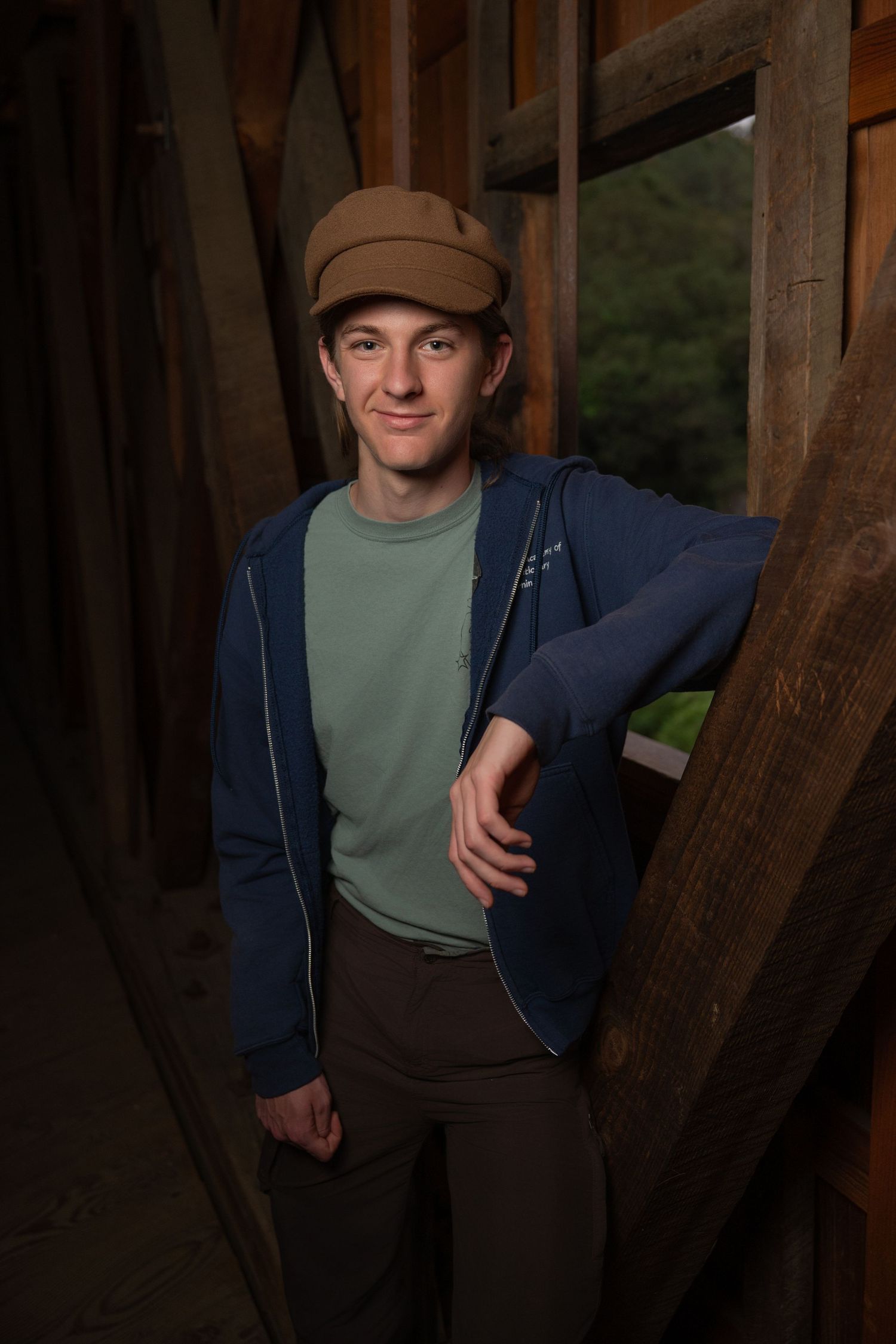 A senior Boy photo taken at Penn Valley, California.  He wears a brown cap and is in front of a window opening inside a covered bridge.