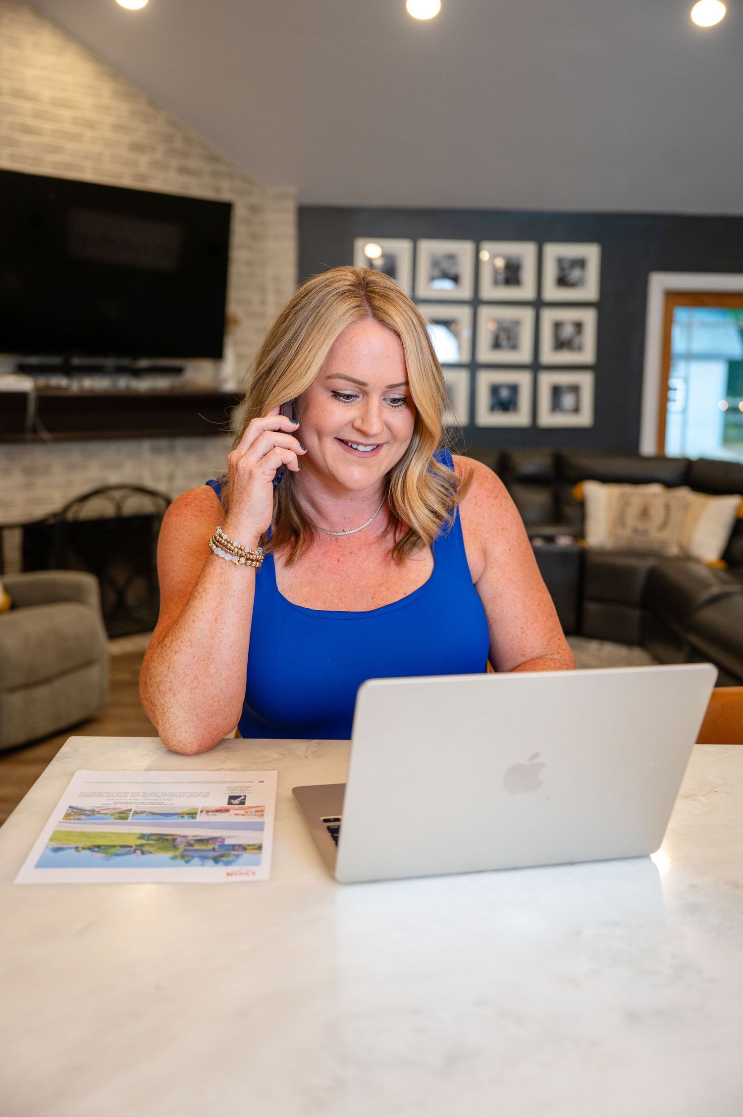 Personal branding photo of a female realtor sitting at her breakfast bar in front of a laptop while chatting on her cell phone.