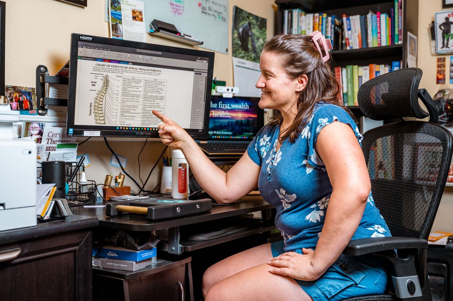Personal Branding Photo of a Naturpathic Health Practitioner in her office pointing to her computer monitor that has a diagram of the spine