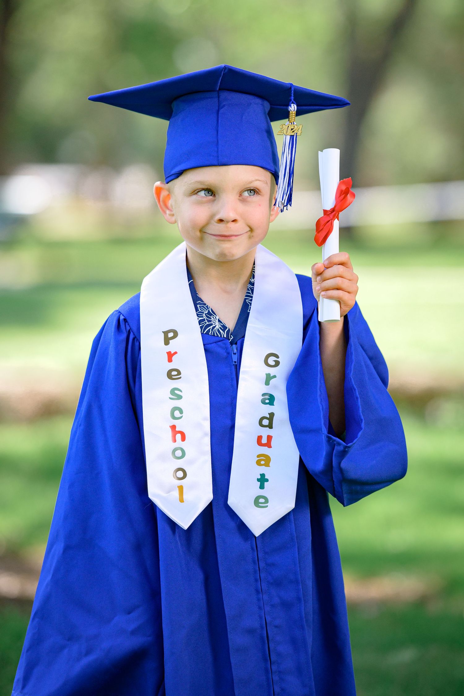 A Preschool Graduate wearing a cap and gown and a sash that has the words 