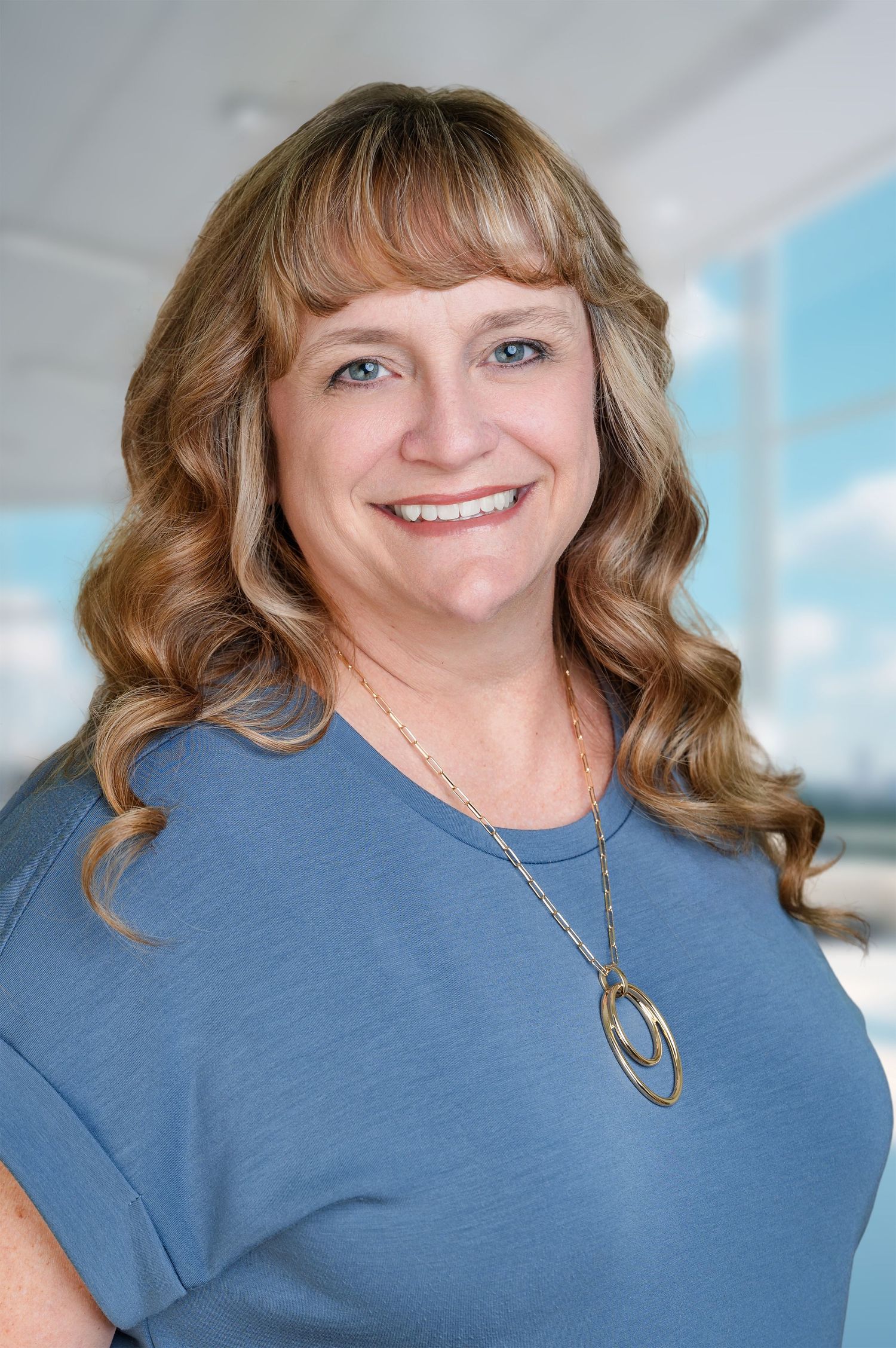 Headshot with an office background that has lots of windows and blue skies outside the windows.