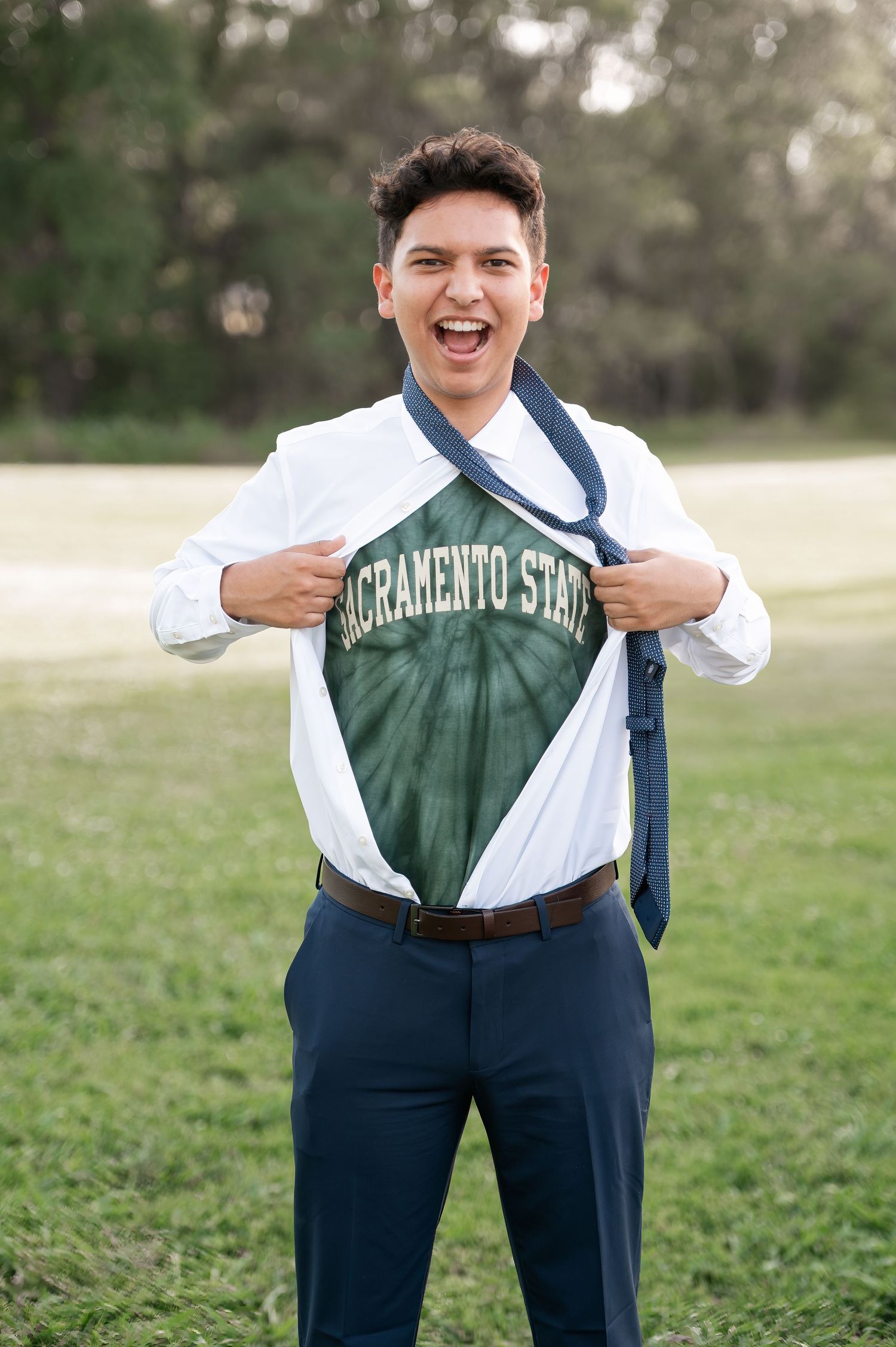 Senior Boy wearing a white button down shirt that's opened to reveal his Sacramento State shirt underneath, Superman style.