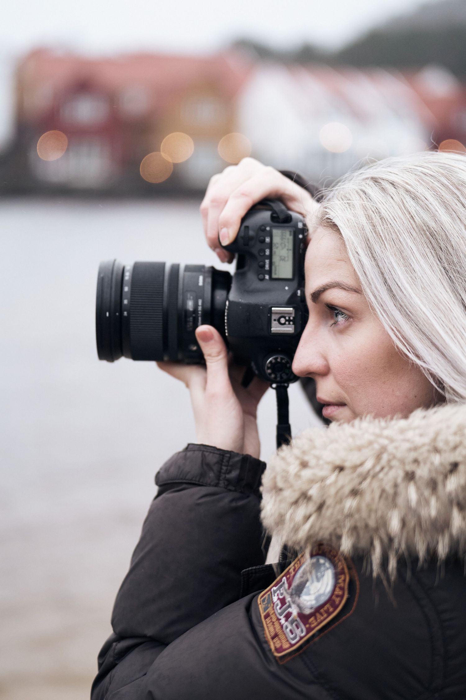 Fotograf på Sørlandet. Kamilla Haaland fotograferer portrett utendørs med hav og hytter i bakgrunnen.