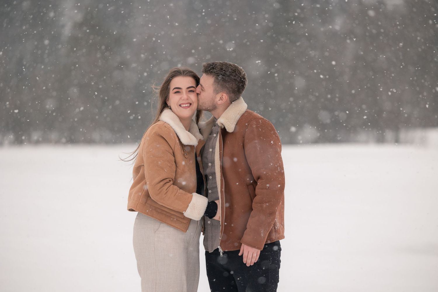 Forlovelsesbilder/kjærestefotografering. Kjærestepar i snøvær. Mannen kysser sin fremtidige brud på kinnet.