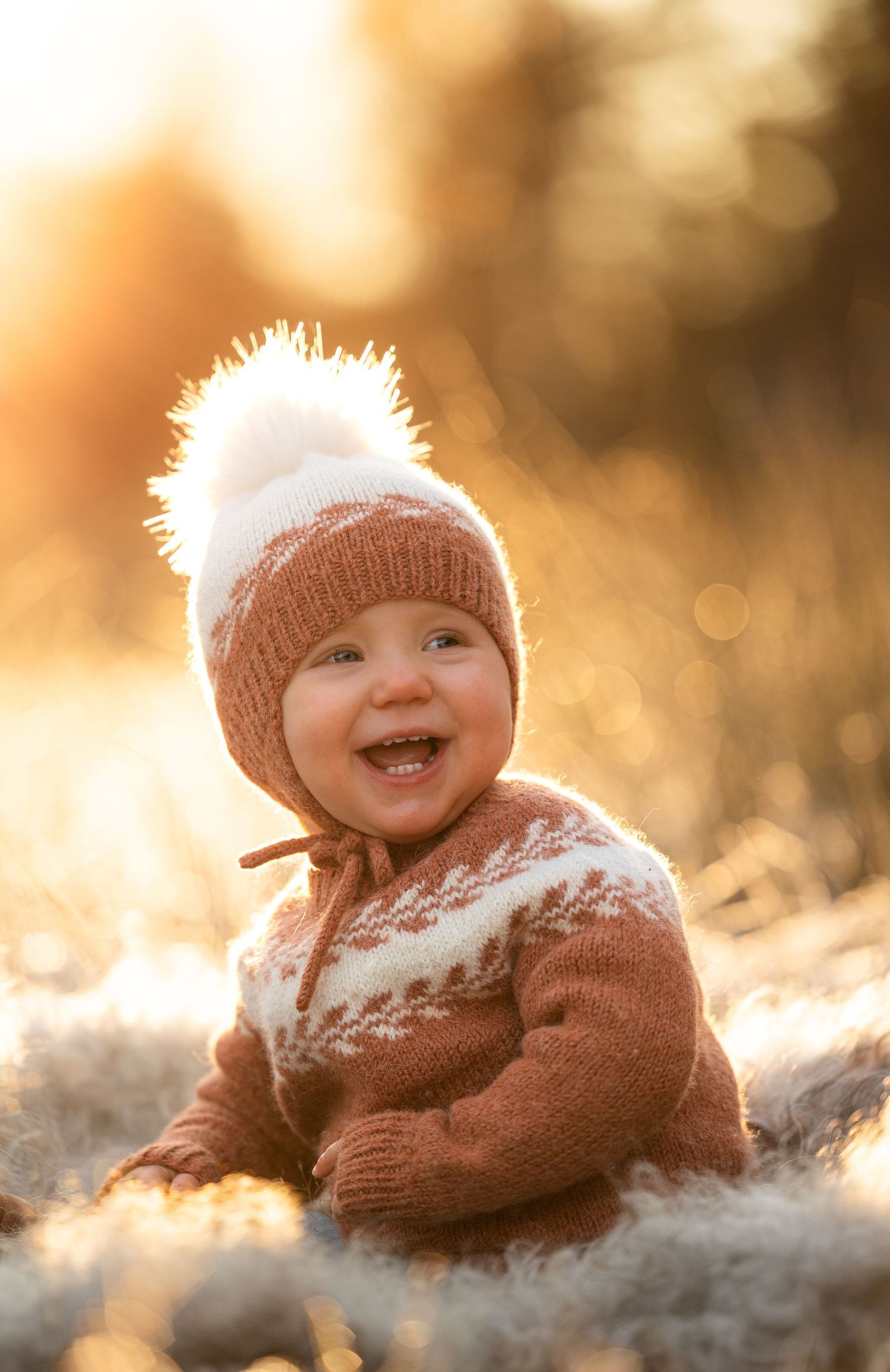 Ettårsfotografering i golden light på Sørlandet. Ei jente i ført strikketøy og stort smil i fokus. Nydelig bookeh. Barnefotografering.
