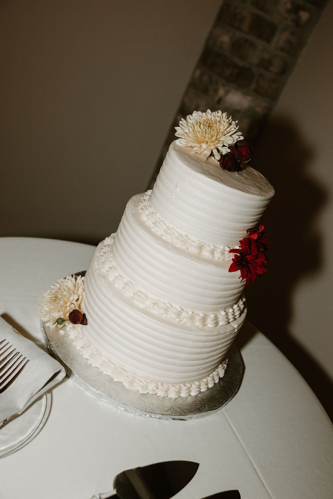 A three-tiered white wedding cake decorated with chrysanthemums and red floral accents.