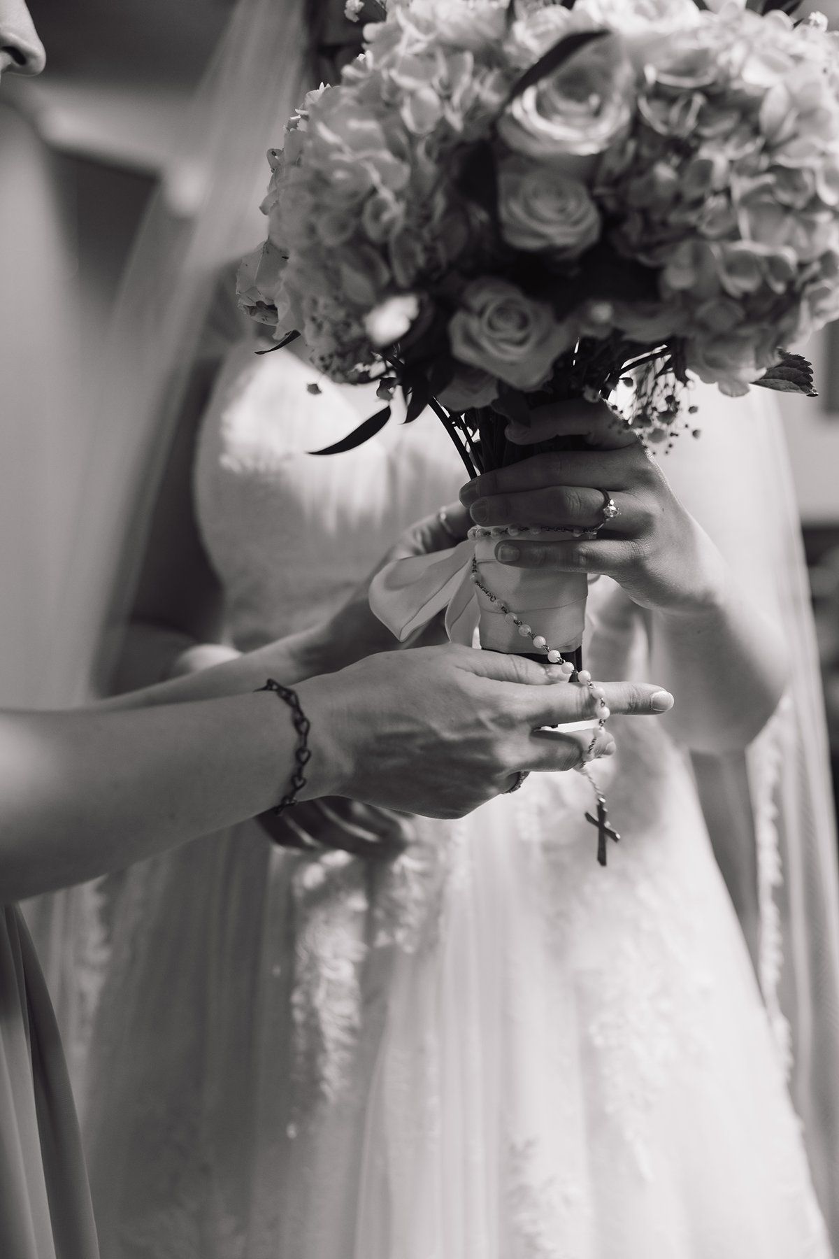 Black and white photo showing hands holding elegant bridal bouquets with roses against white wedding dresses.