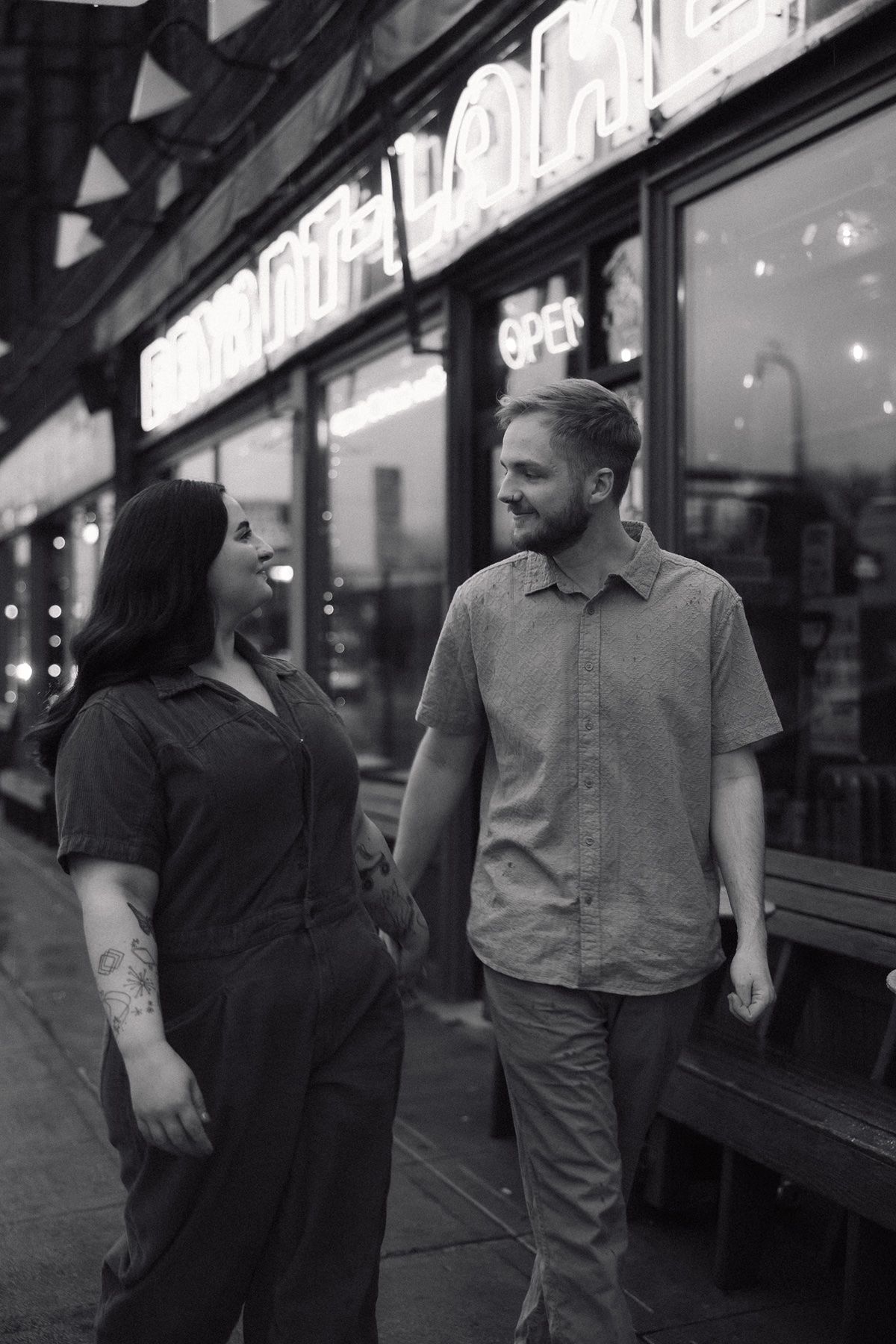 A couple walking together outside a storefront with illuminated signage at night.