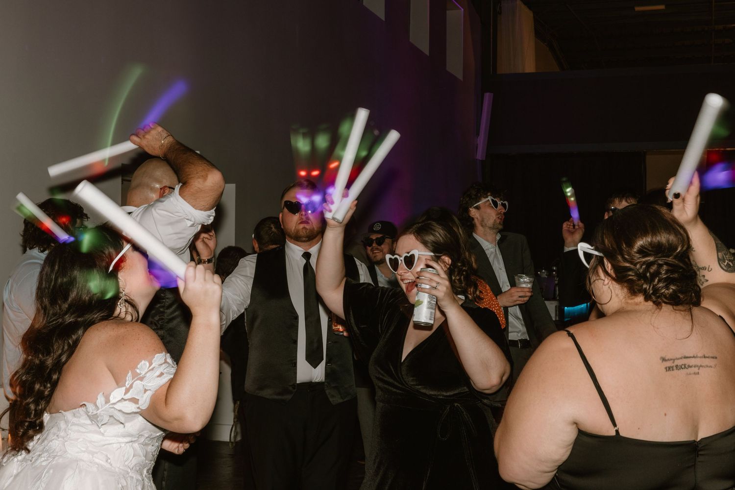 People dance and wave colorful LED light sticks at a dimly lit reception party.