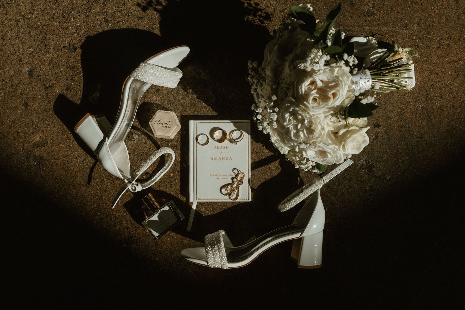 Wedding accessories including white heels, rings, and a delicate floral bouquet arranged on a dark background.