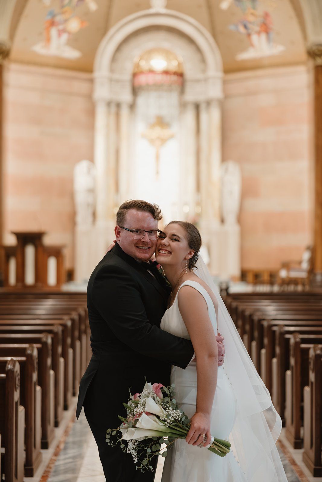 Newlywed couple shares intimate moments in a beautiful cathedral with ornate arches and wooden pews.