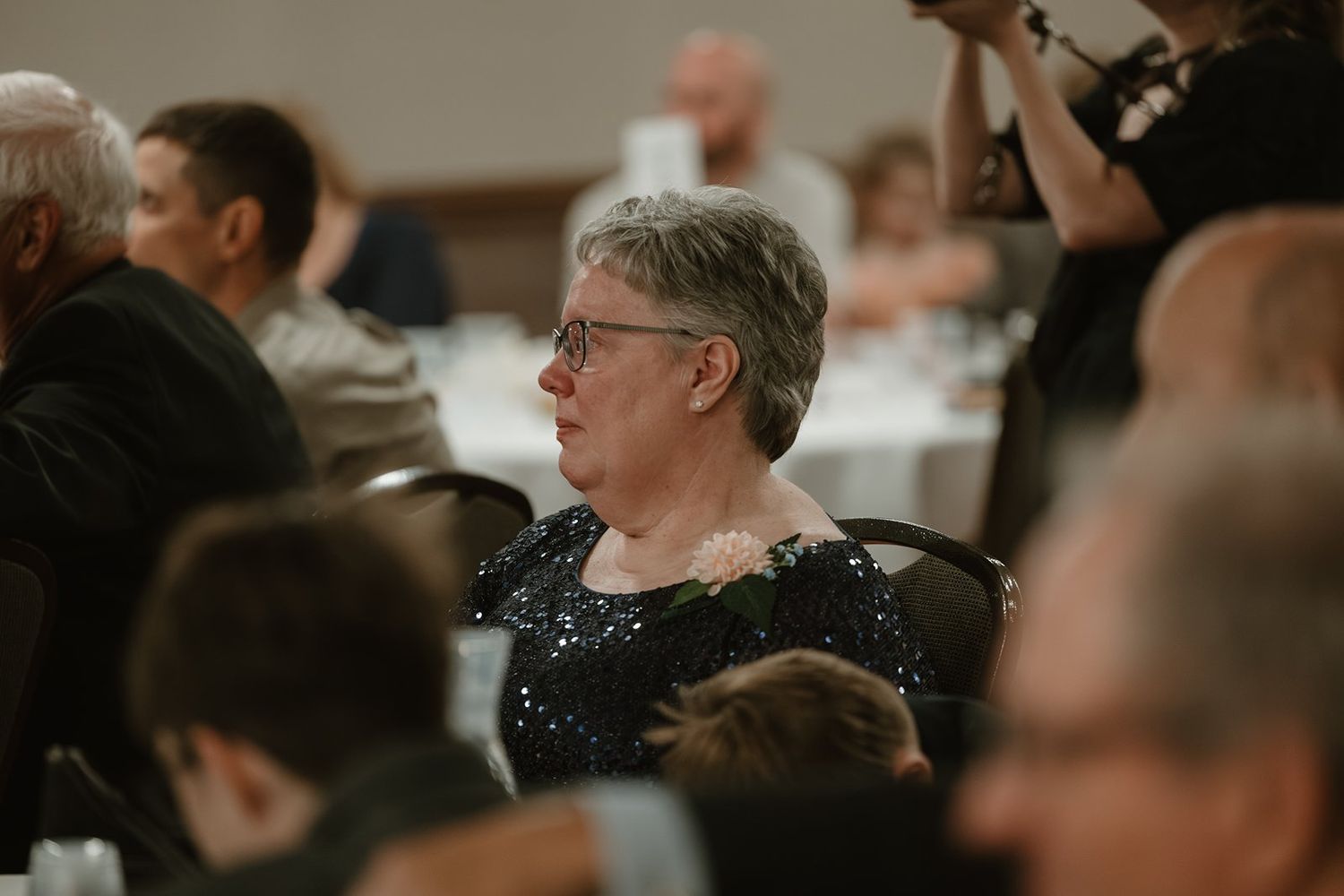 People sit in rows at a formal event or ceremony while someone stands at the front addressing the audience.