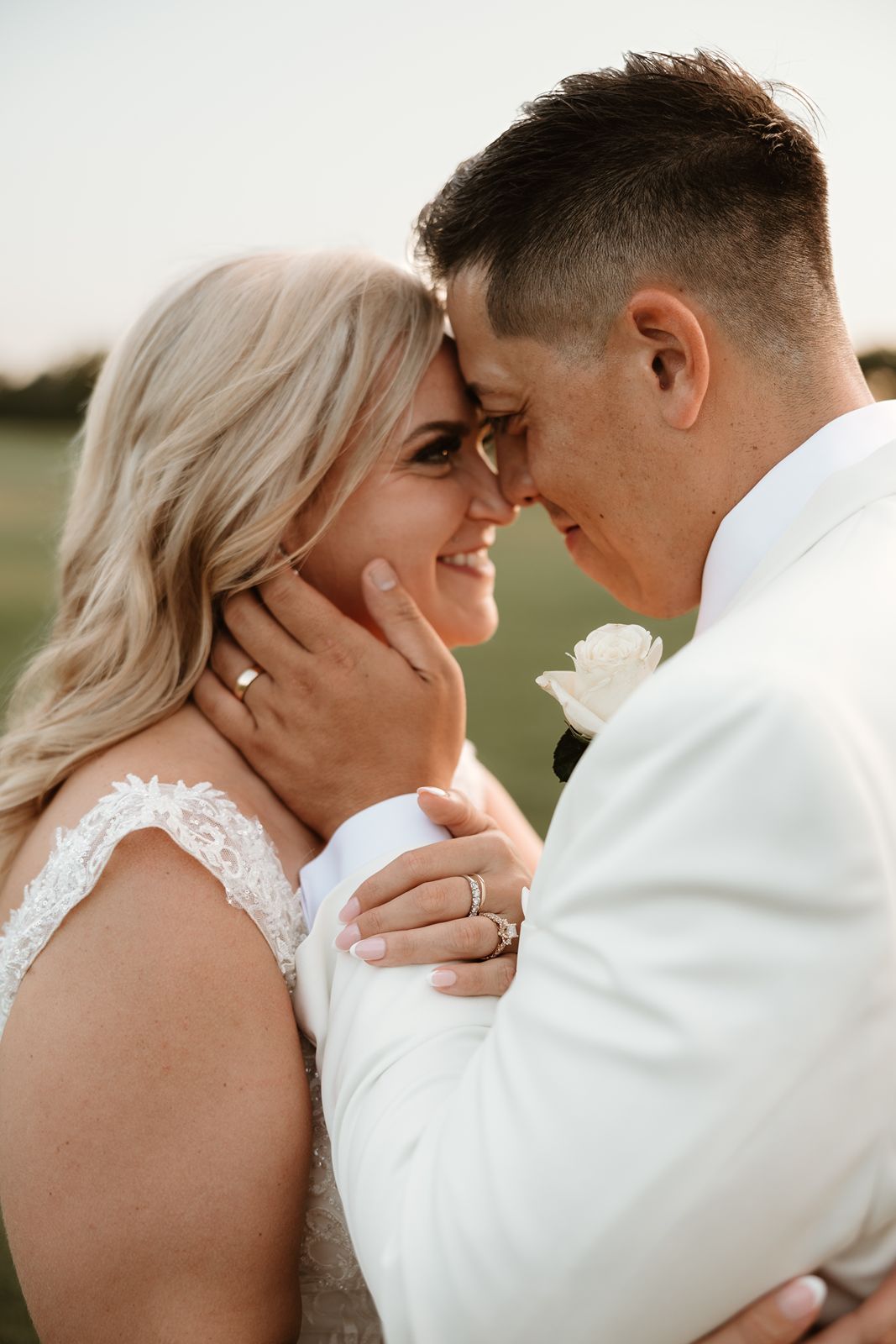 A romantic wedding portrait of a couple in white sharing an intimate moment outdoors.