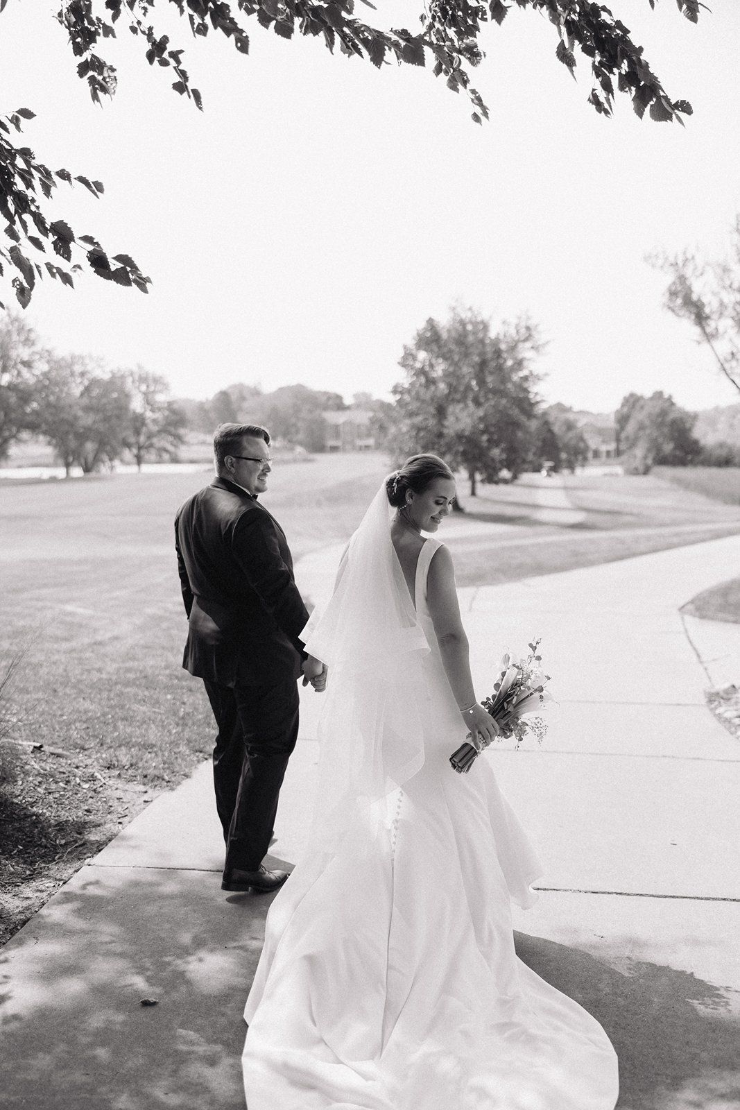 A couple in wedding attire walks down a path together in a series of black and white photos showing different angles.