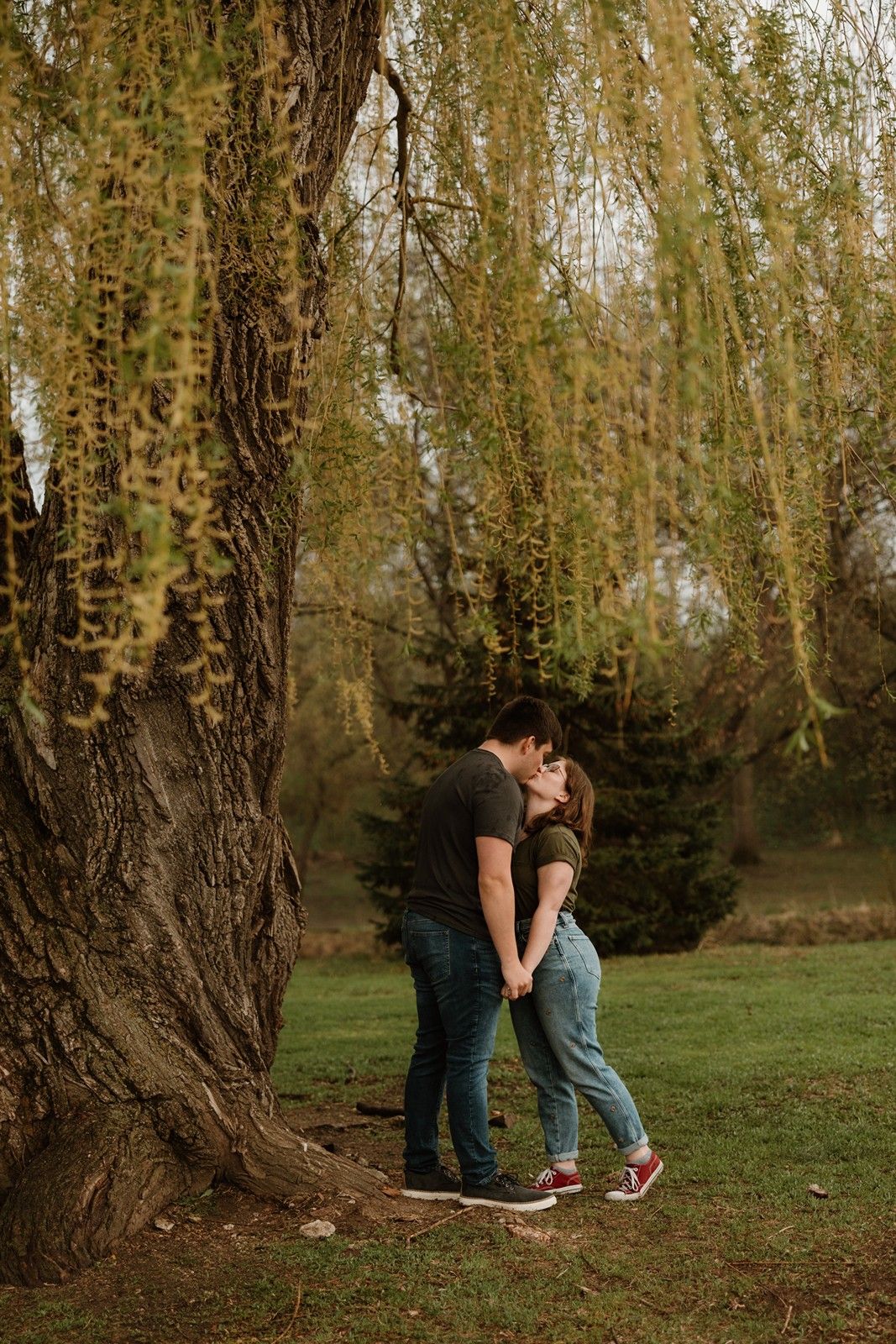 Romantic couple sharing an intimate moment beneath willow trees in a natural outdoor setting.