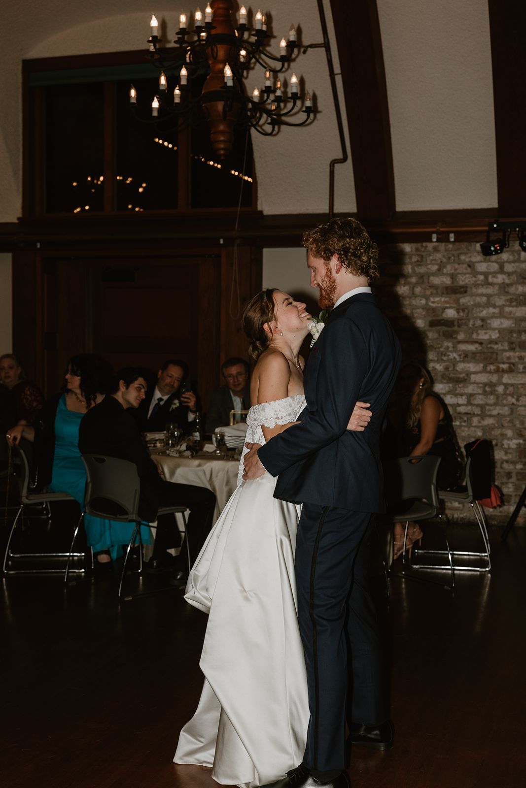 A couple shares their first dance in an elegant reception venue with chandeliers.