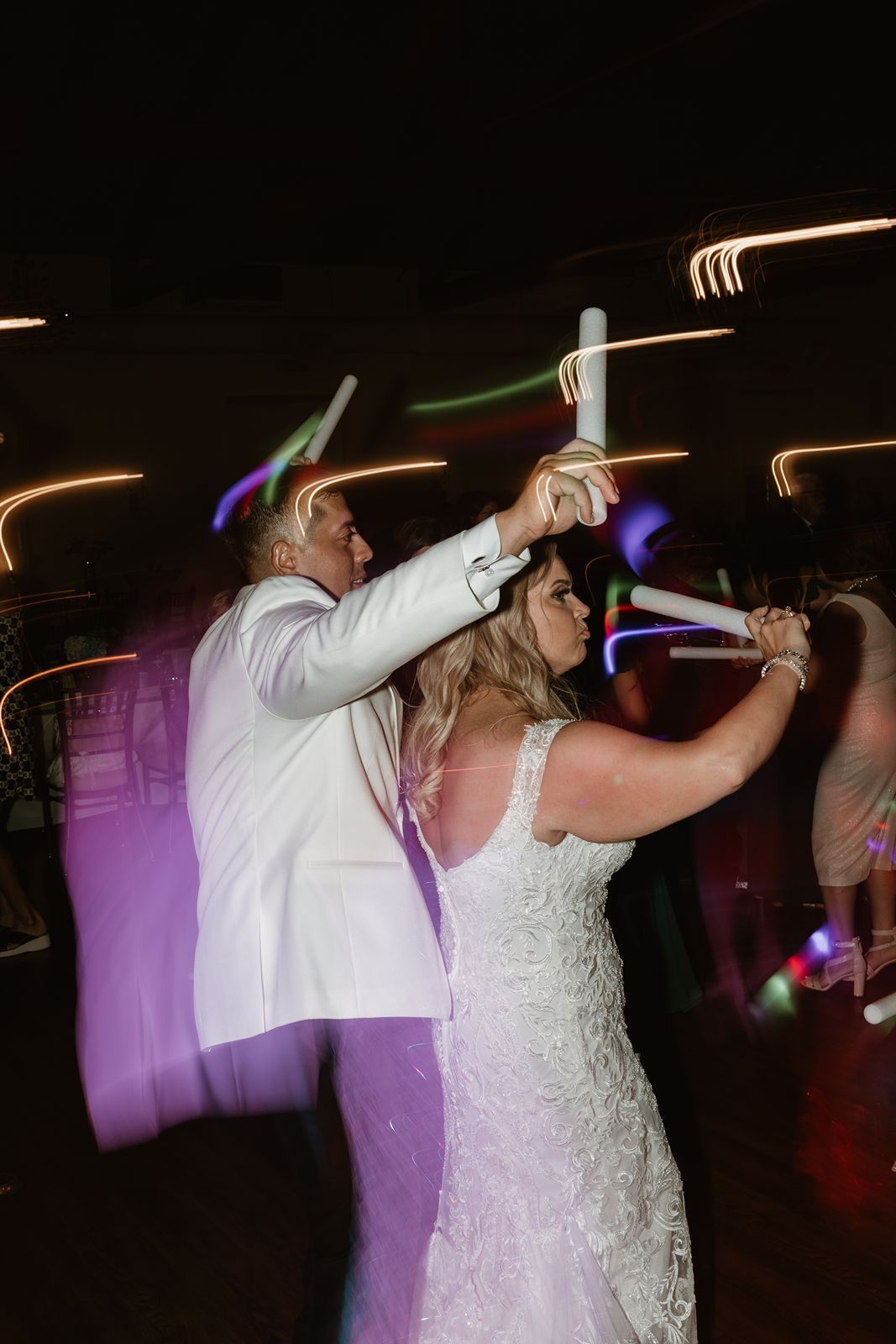 Wedding celebration with LED light sticks creating colorful light trails on the dance floor.