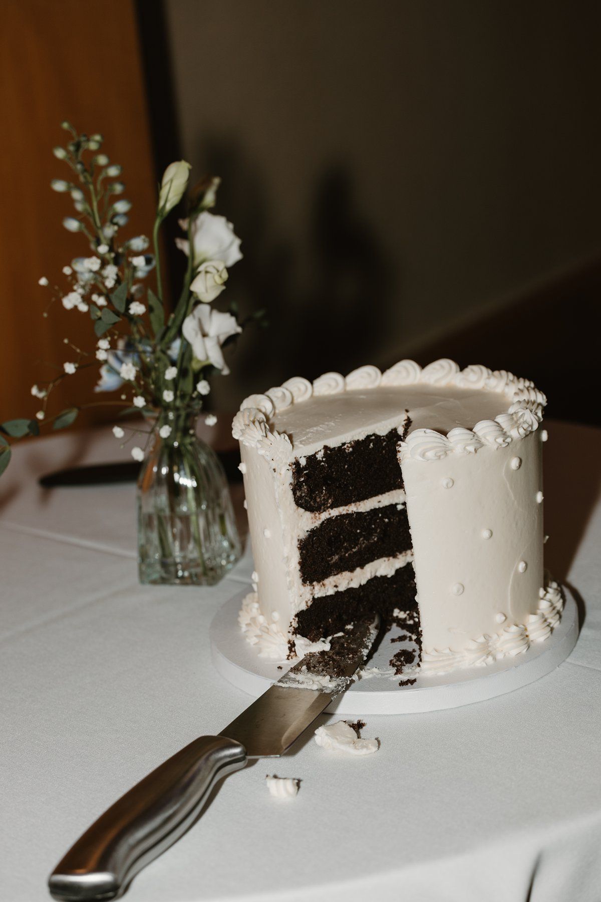 A white wedding cake with black layers is cut into slices on a table with delicate floral decorations.