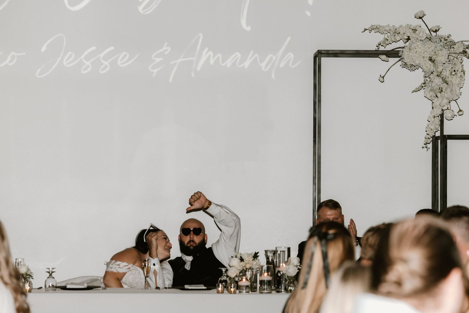 Wedding reception guests at a banquet table raise their glasses during a celebration toast.