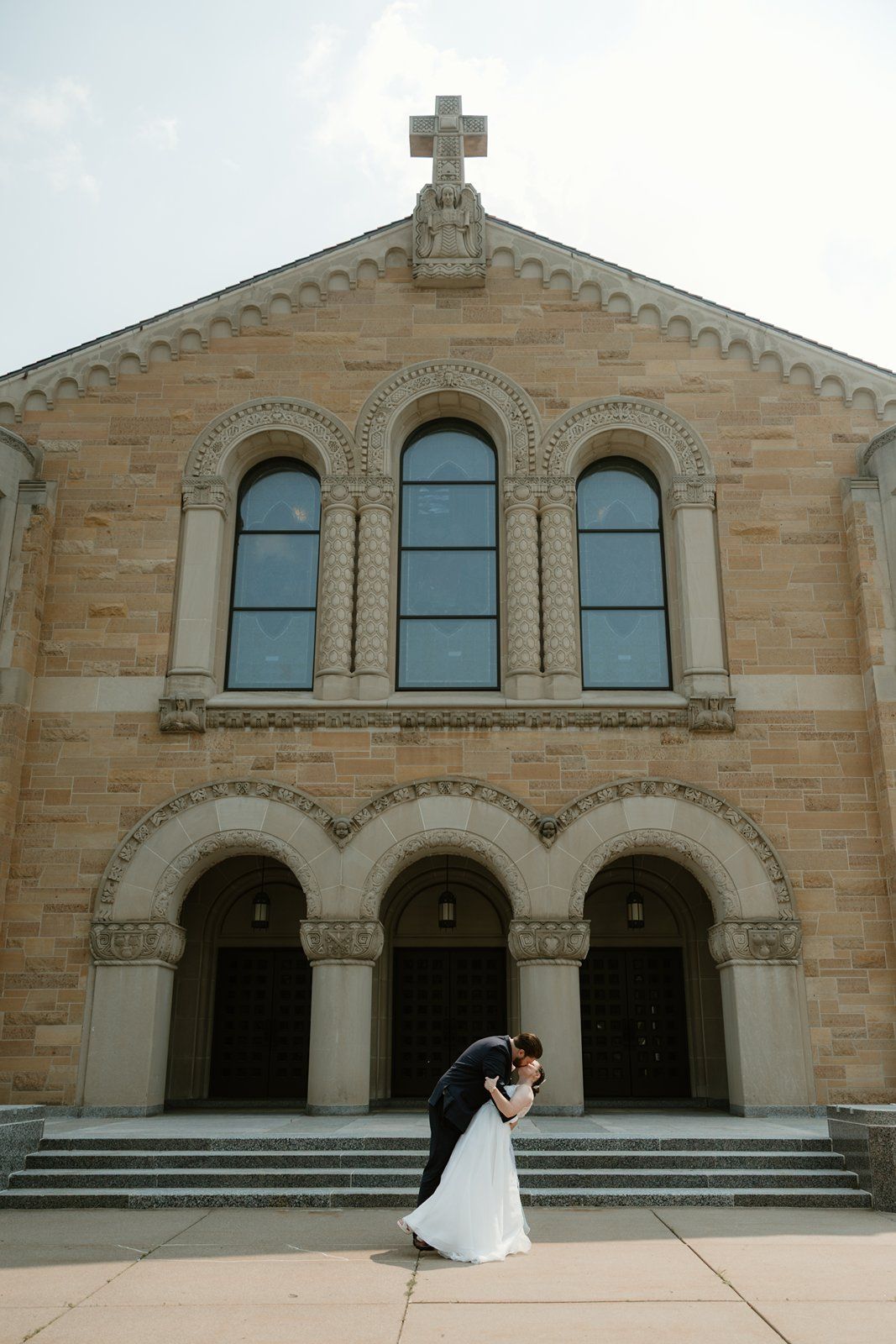 Beautiful stone church exterior with arched doorways and windows provides backdrop for wedding photography.
