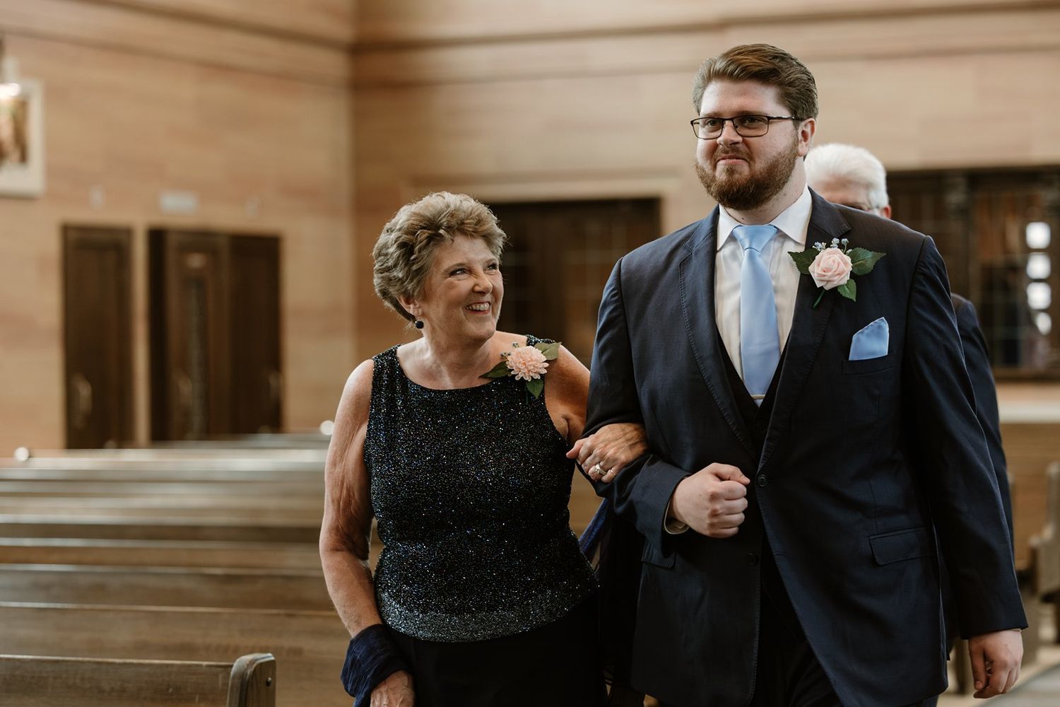 Wedding guests mingle and socialize in a church interior with warm lighting and wooden pews.