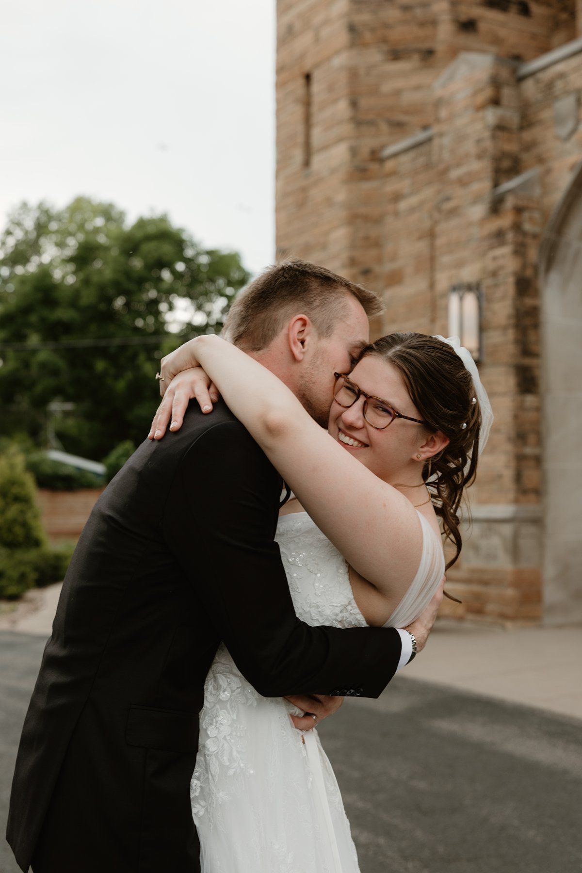 A loving embrace between newlyweds in front of a stone church on their wedding day.