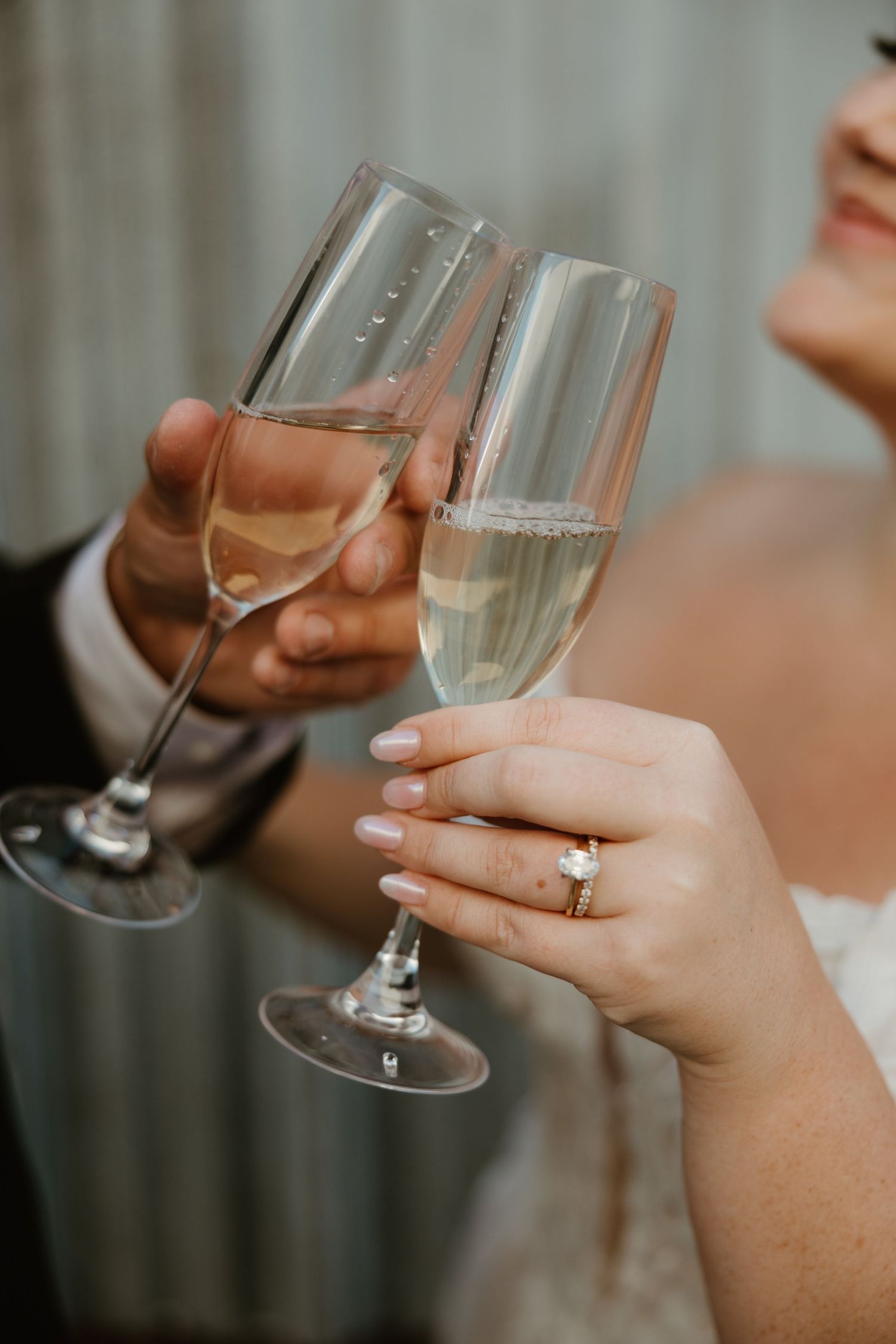 Close-up of champagne flutes clinking in a toast while showing elegant engagement ring during celebration.