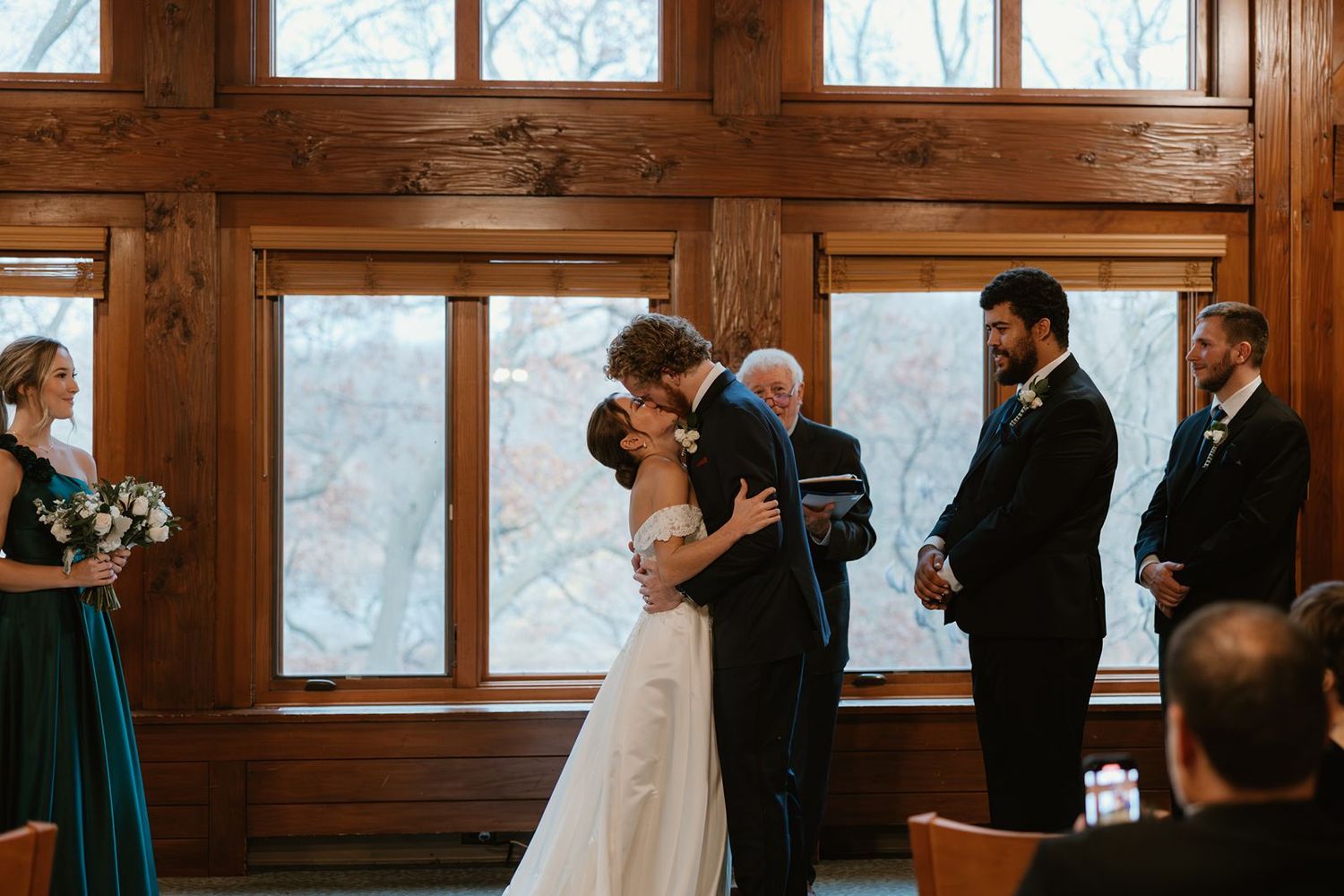 A wedding ceremony takes place in a rustic wooden chapel with large windows.