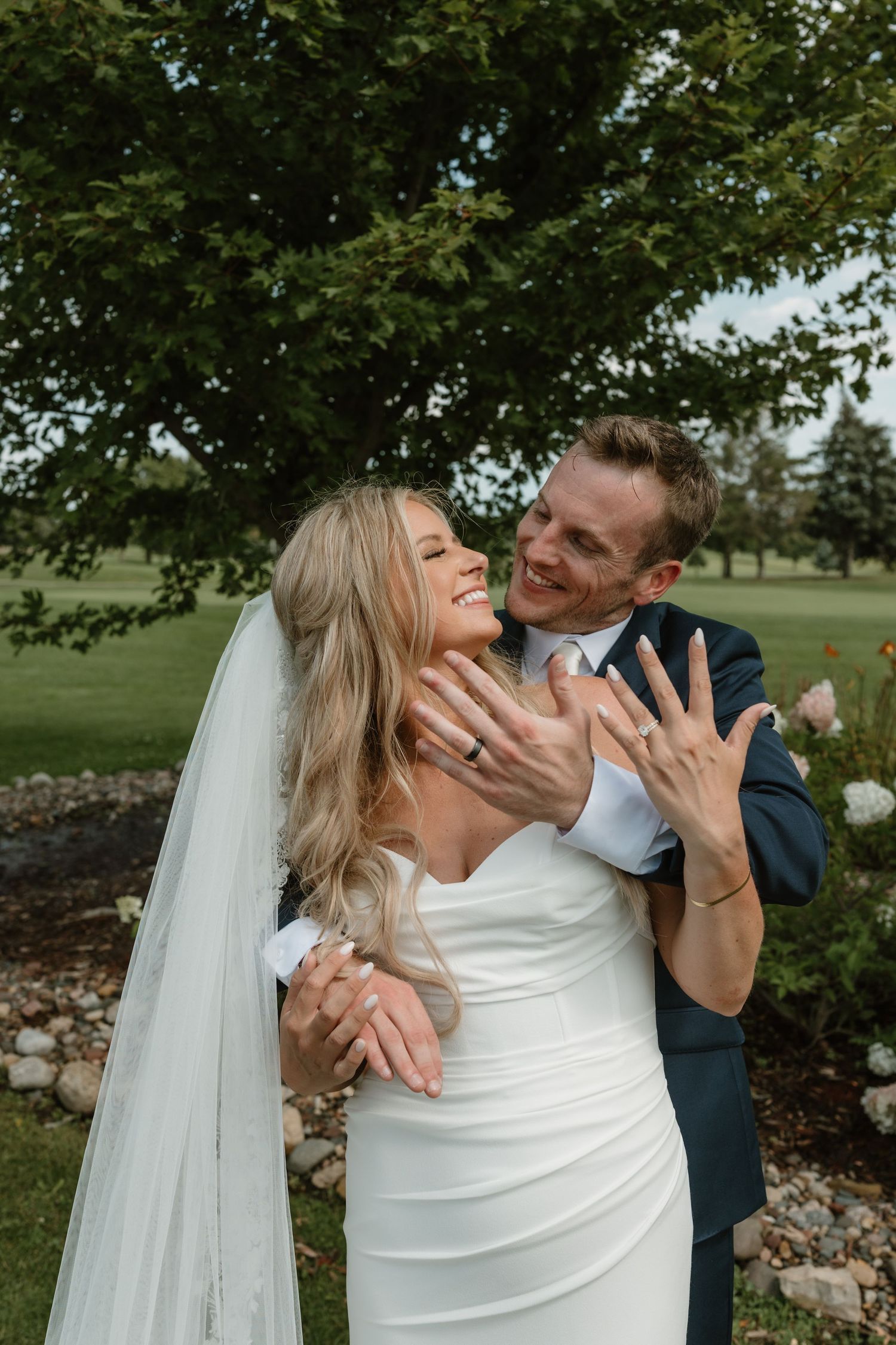 A couple shares playful and romantic moments outdoors during their wedding photoshoot in a garden setting.