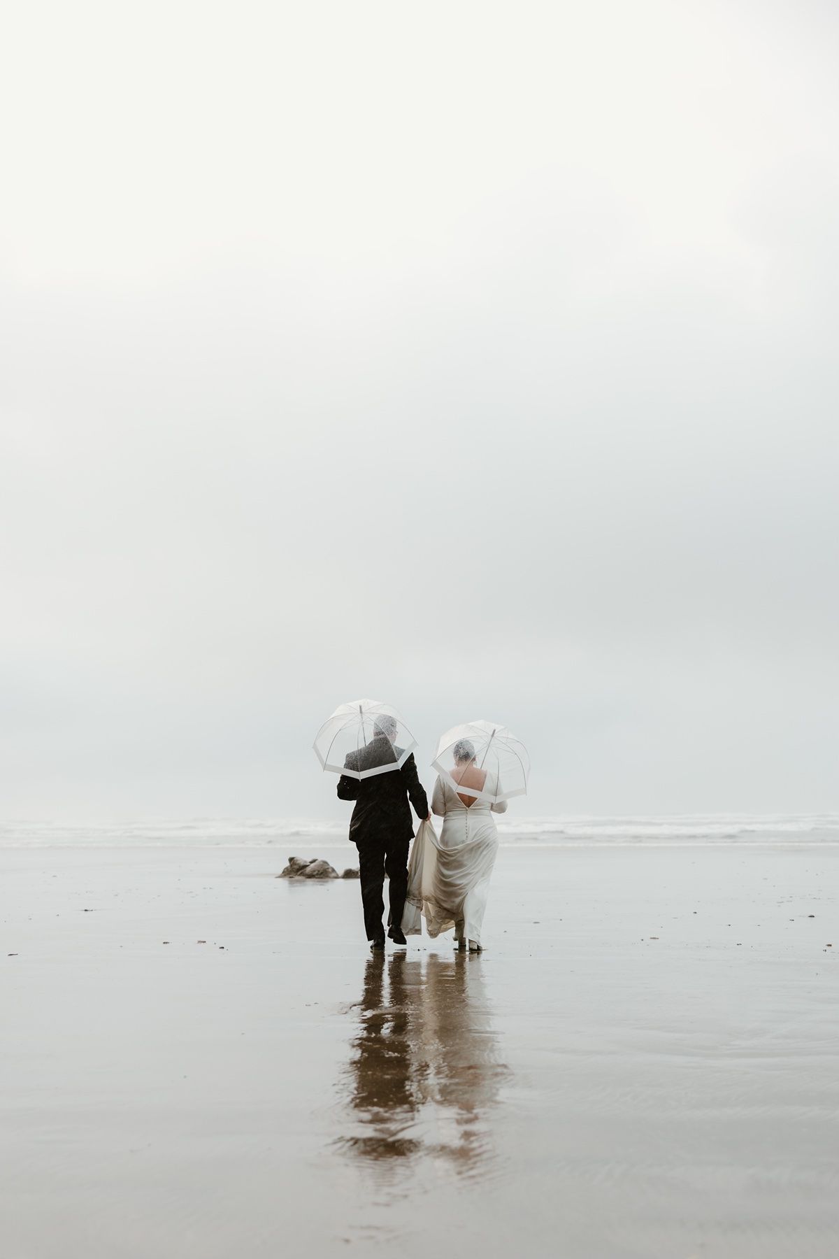 Adventure elopement photographer photographing a couple wrapped in the ocean breeze on the coast during a rainy winter day