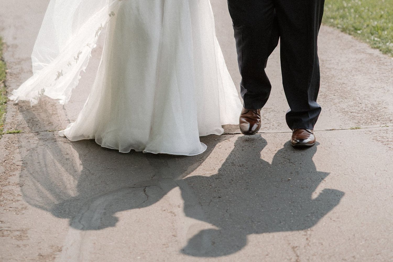 Bride and groom's feet shown walking together on a path, with the bride's white dress flowing beside them.