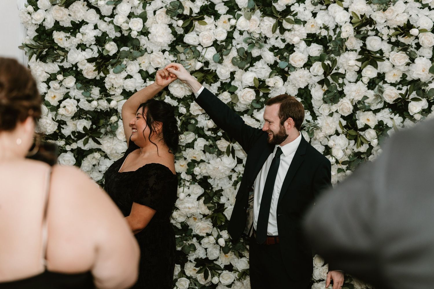 Two people dancing together in front of a stunning white flower wall backdrop at an elegant event.