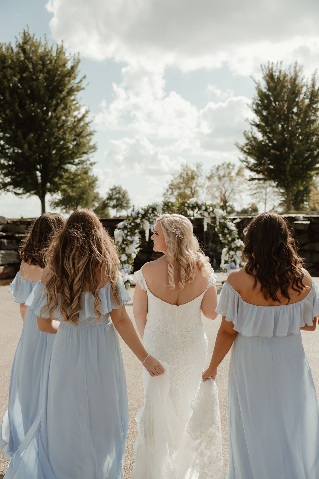 Back view of bride and bridesmaids holding hands in light blue off-shoulder dresses.
