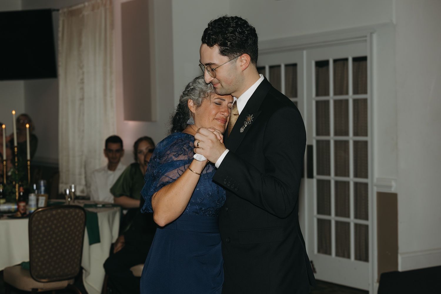 Groom dancing with mother in blue dress at wedding reception in elegant venue.