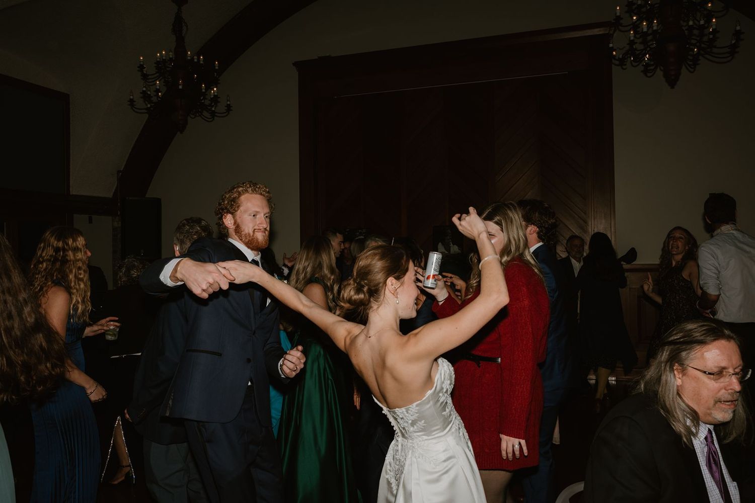 Wedding guests dancing and celebrating on a dimly lit dance floor during the reception.