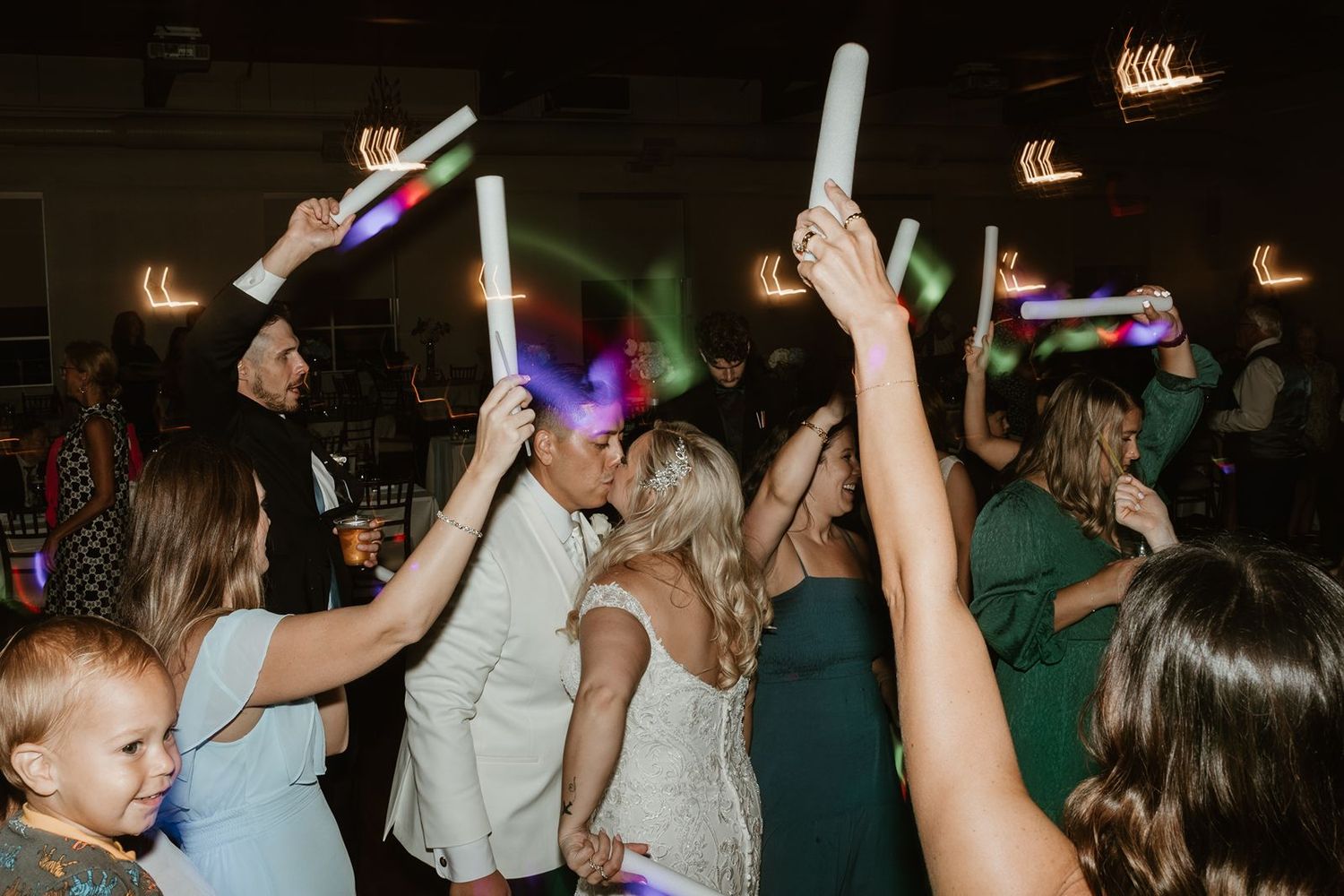 Guests celebrate with glowing LED sticks on a dimly lit dance floor at a wedding reception.