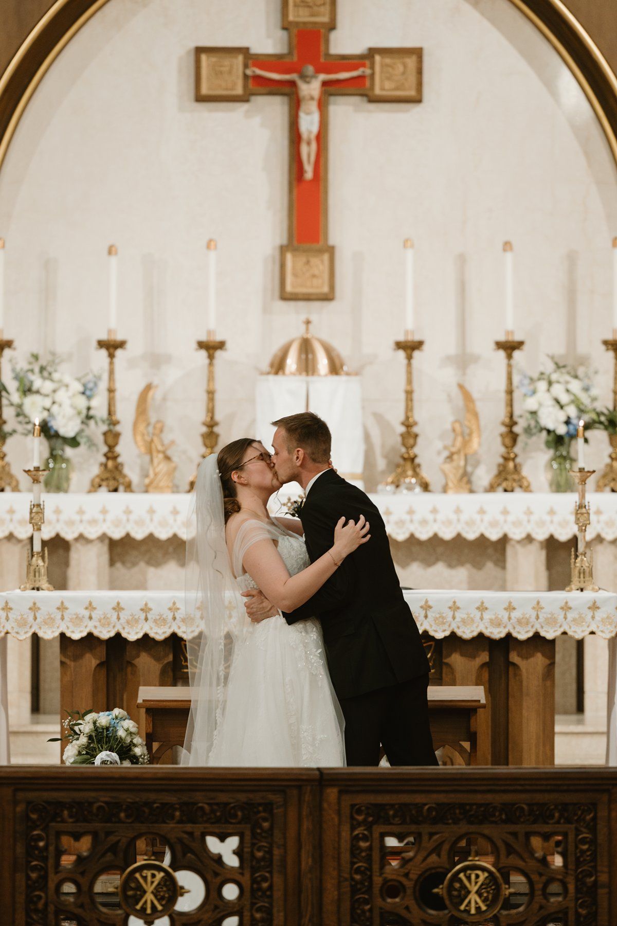 A wedding couple shares an intimate moment at the altar of a Catholic church with a large crucifix and candles in the background.