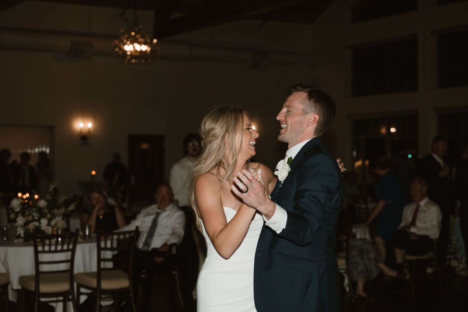 A couple shares their first dance together at a dimly lit wedding reception venue.