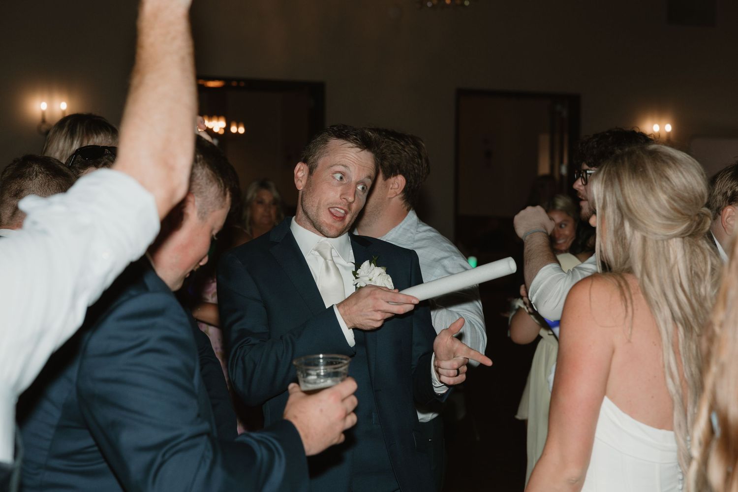 People dancing and socializing at a dimly lit party or celebration with ambient lighting in the background.