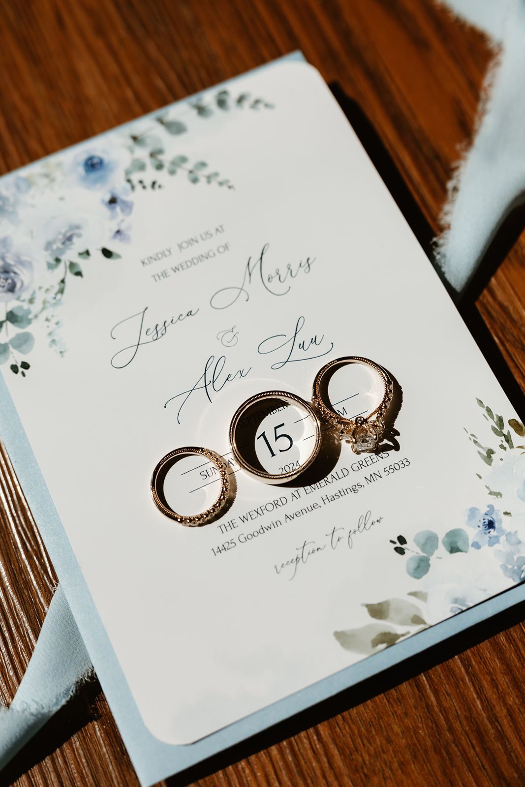 Wedding invitation with floral watercolor design and three engagement rings artfully arranged.