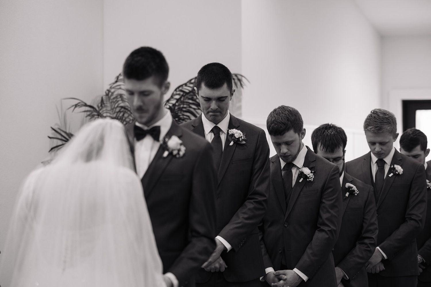 Black and white photo of groomsmen sharing a laugh together during a wedding ceremony.
