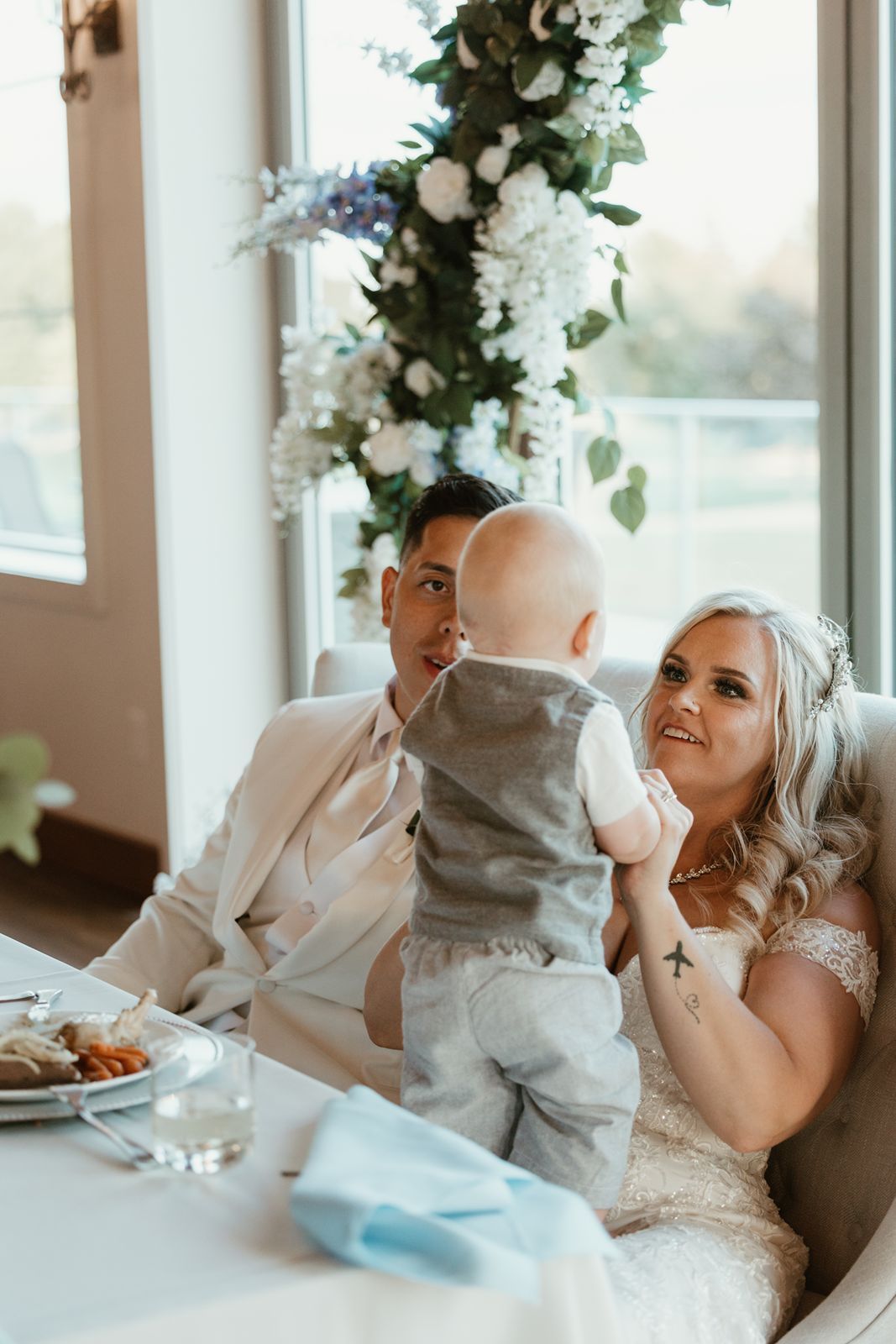 Newlyweds share a tender moment with a baby under floral wedding decorations.