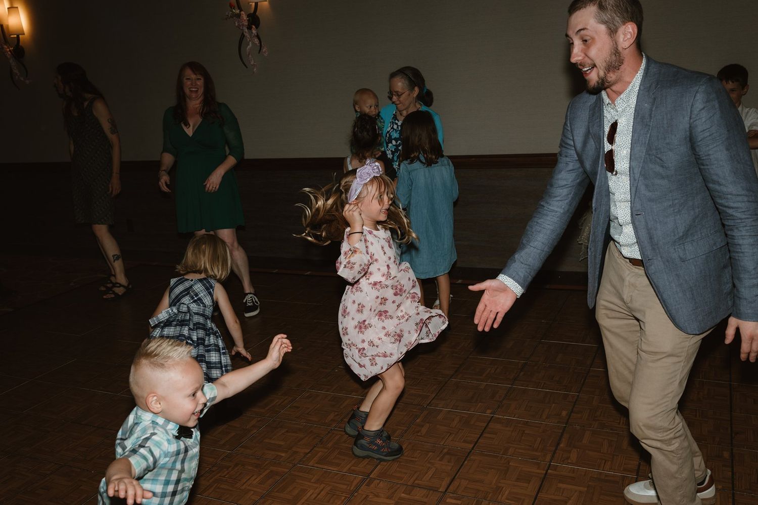 Wedding guests dance and celebrate together on a dark dance floor during an evening reception.