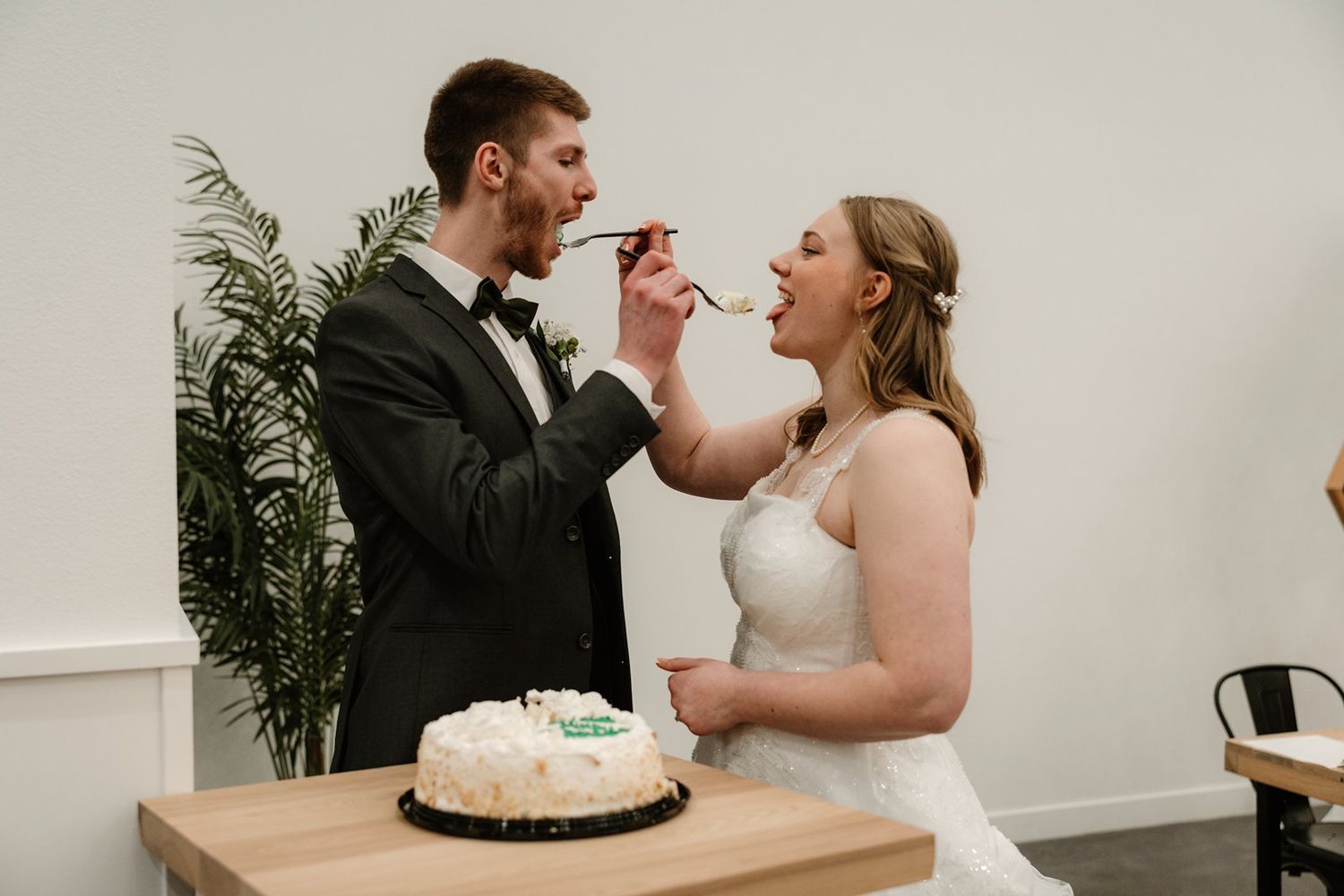 A couple shares a playful moment while feeding each other wedding cake at their reception.