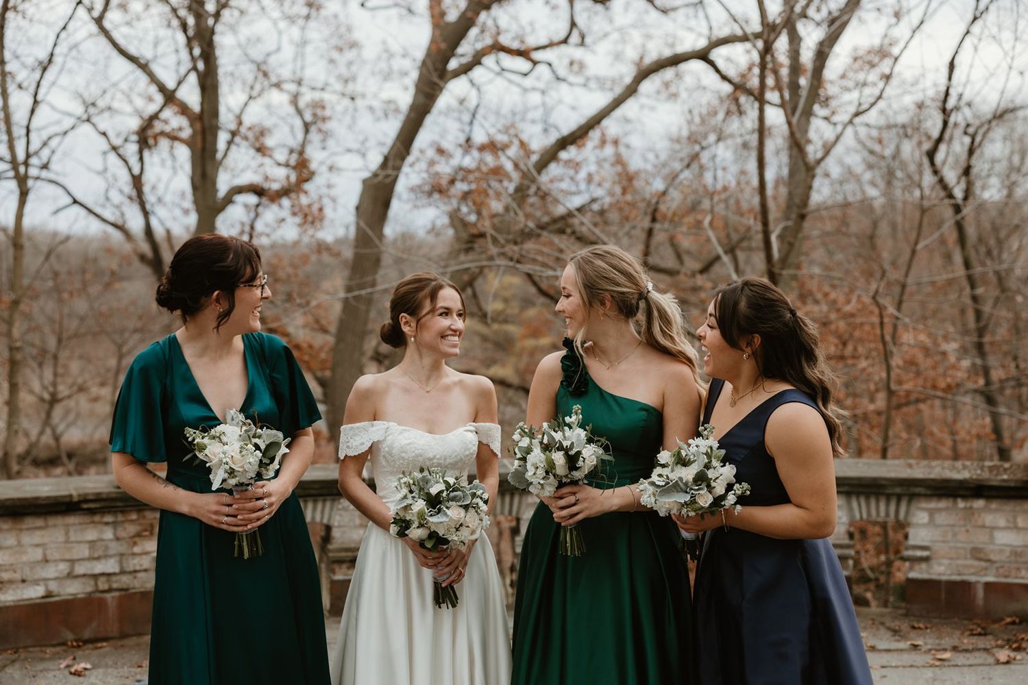 A bridal party in emerald green dresses poses together holding white bouquet on the Tea Room Terrace.