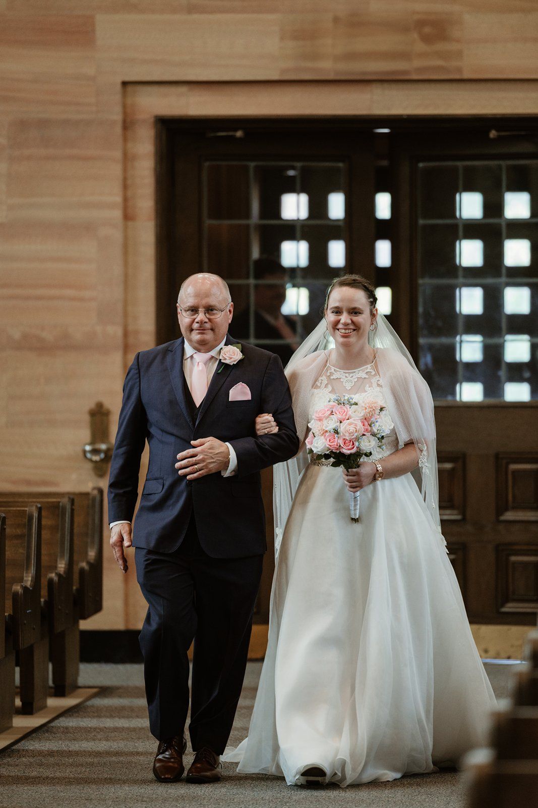 A wedding ceremony procession walking down the aisle of a traditional church with wooden pews.