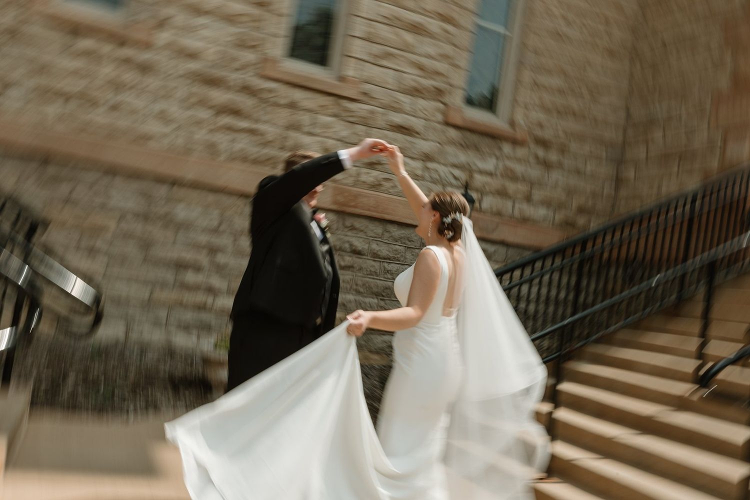 A bride in a flowing white wedding gown walks down stone stairs in an elegant venue.
