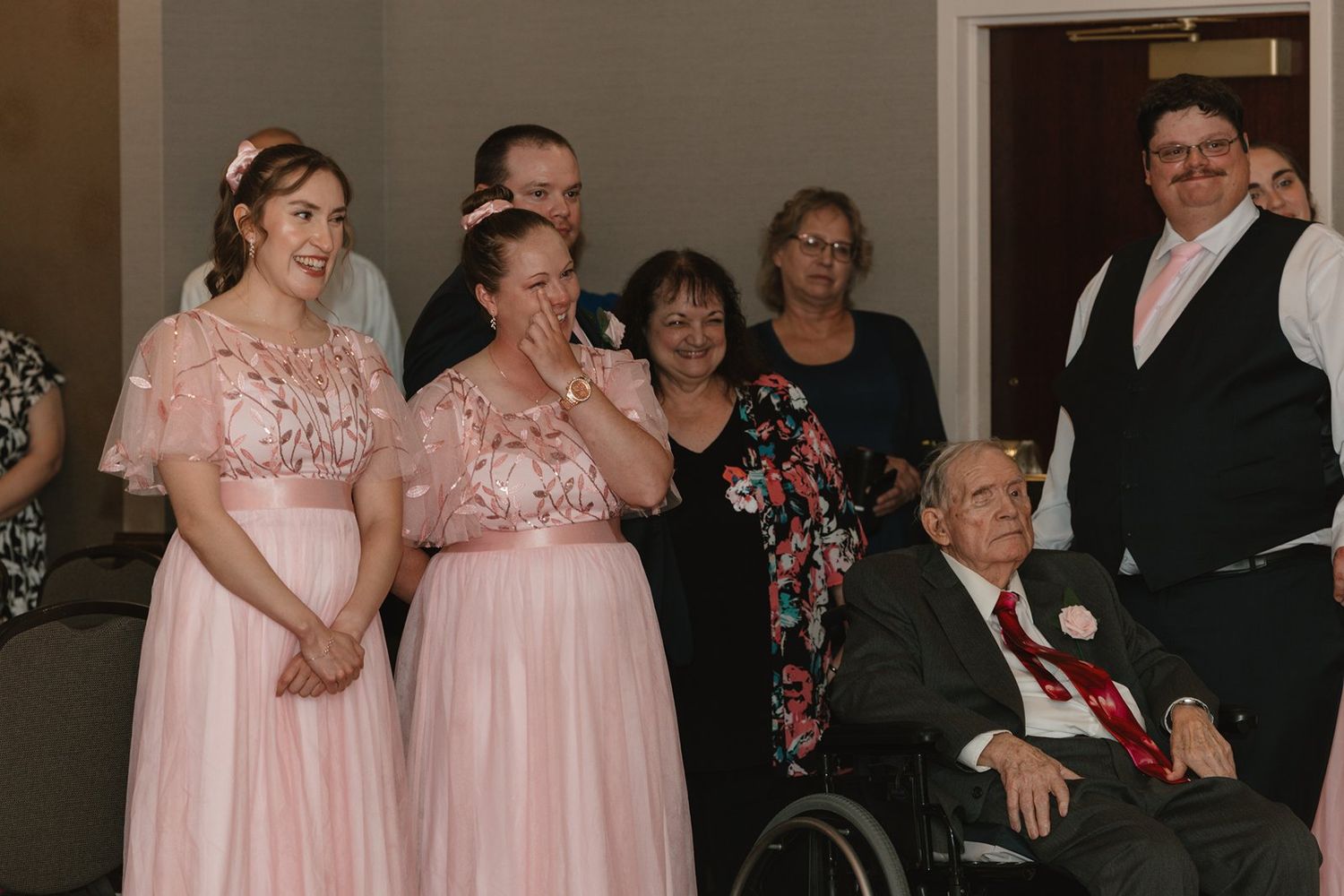 Wedding guests in formal attire gather together for a group celebration in an indoor venue.